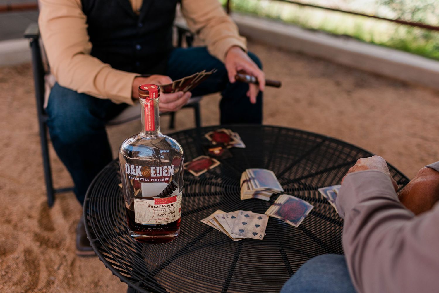 Table scene with bottle of Troy & Sons whiskey and playing cards during outdoor gathering.