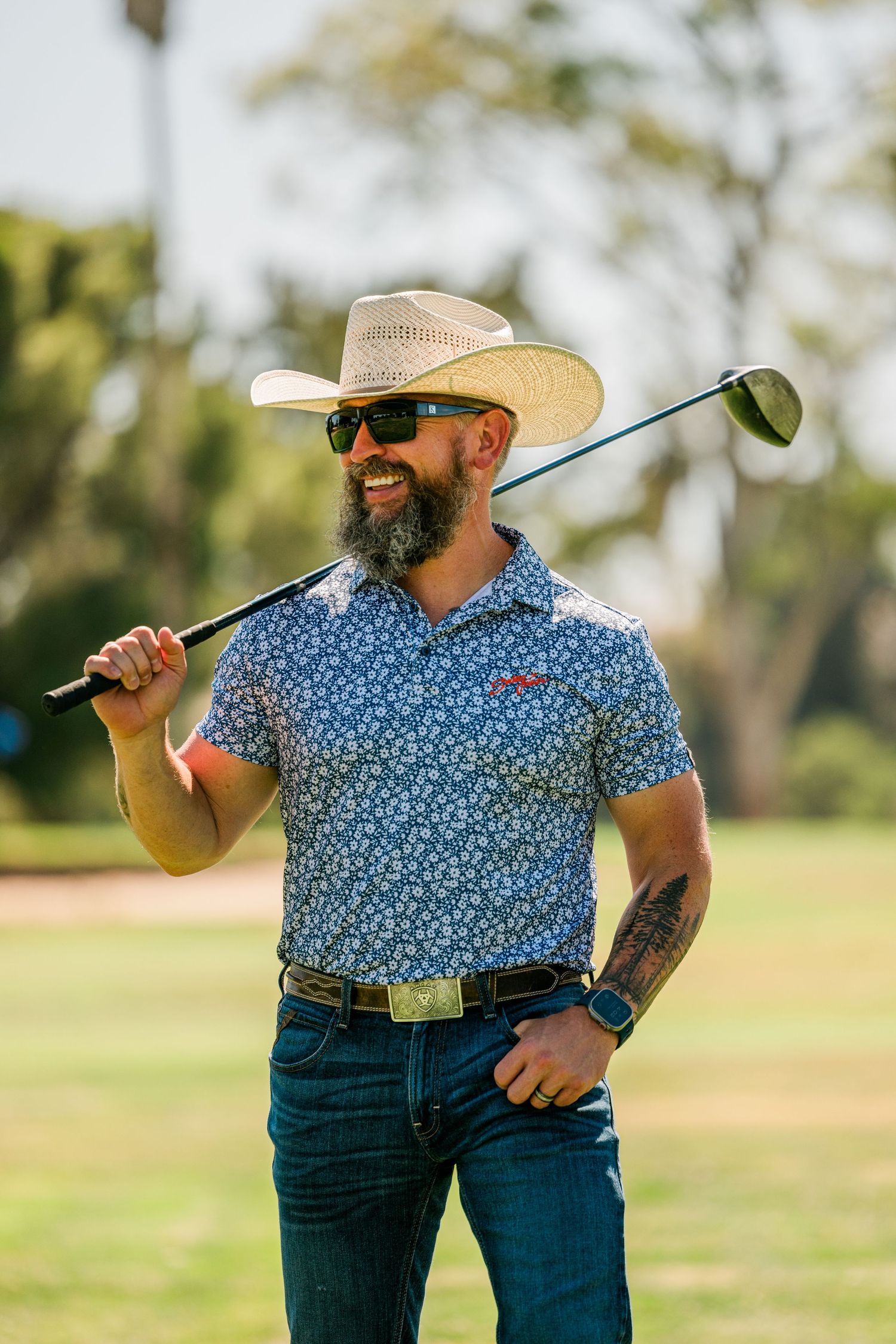 Golfer in western hat and floral polo shirt holding golf club on sunny course.