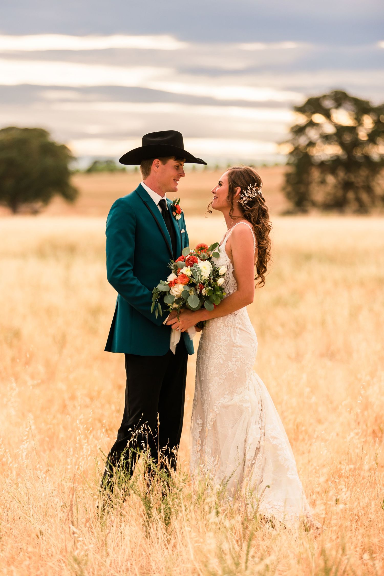 Couple in wedding attire posing in a golden wheat field at sunset with teal accents.