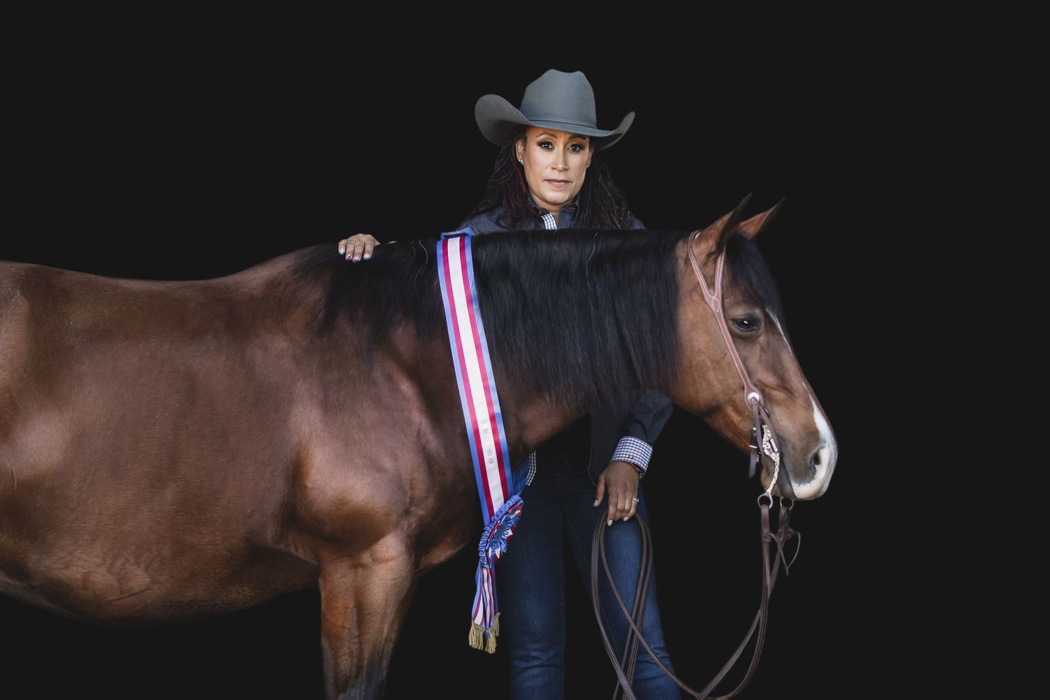Horse in Western show gear stands beside ribbon display against dark background.