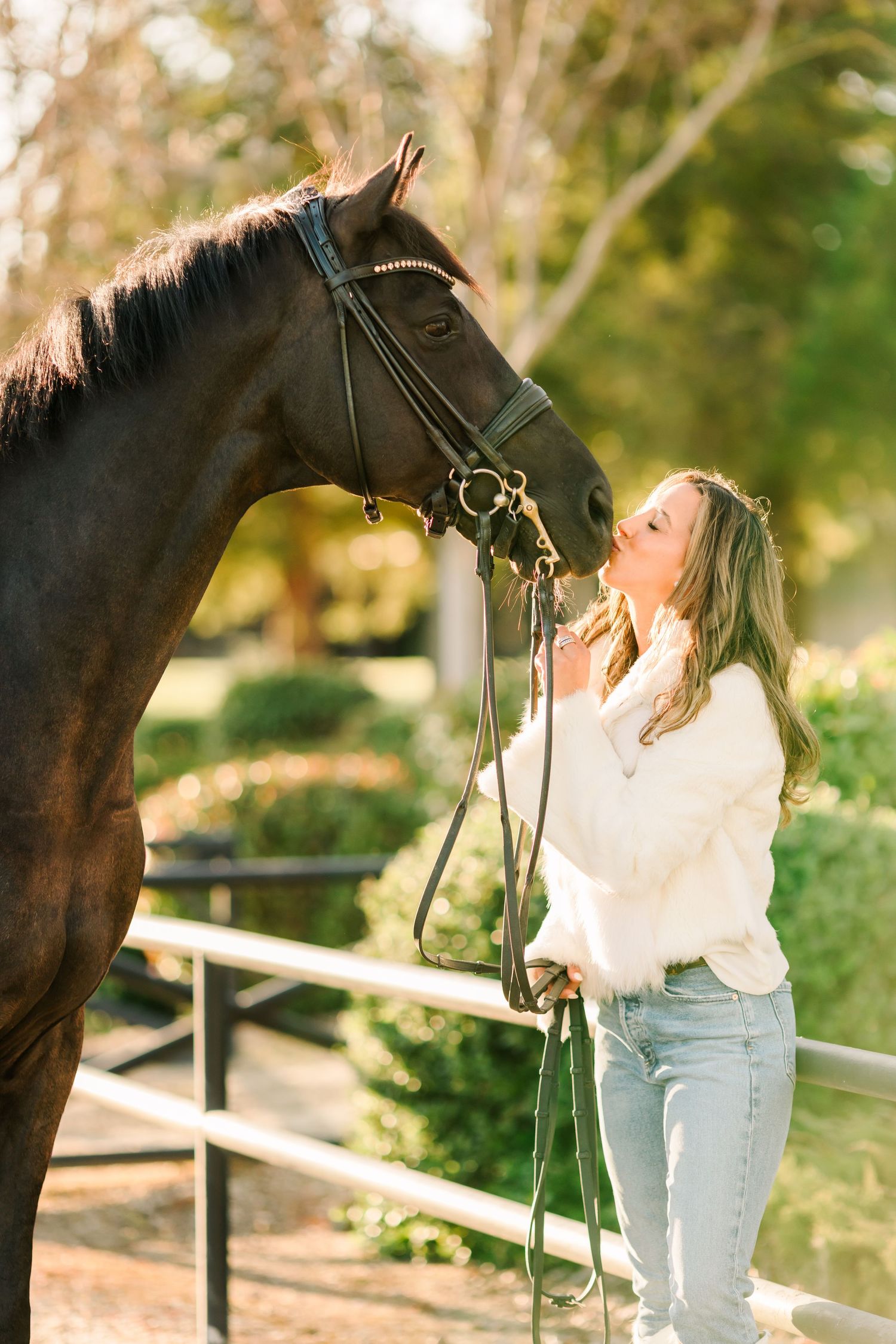 A tender moment between a dark brown horse and a person in white clothing at a wooden fence.