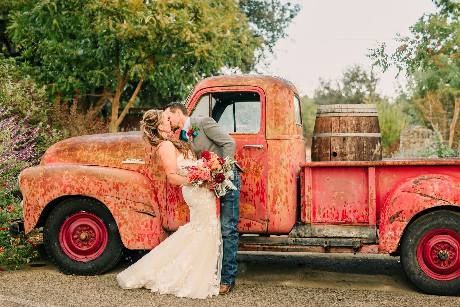 A vintage red truck serves as a rustic backdrop for an elegant wedding photoshoot in an outdoor setting.