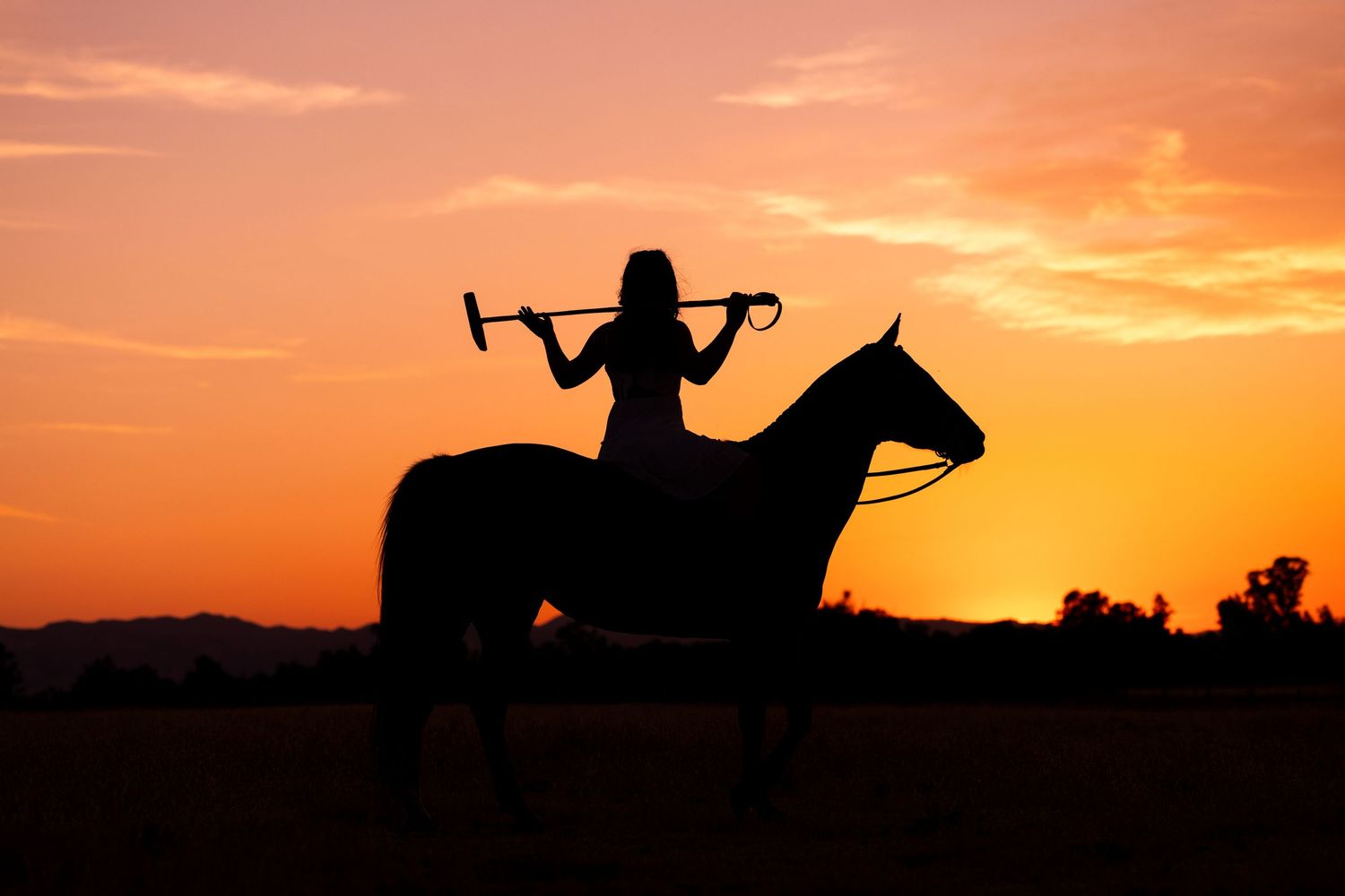 Silhouettes of drones and riders on horseback against vibrant orange sunset sky in a dramatic panoramic view.