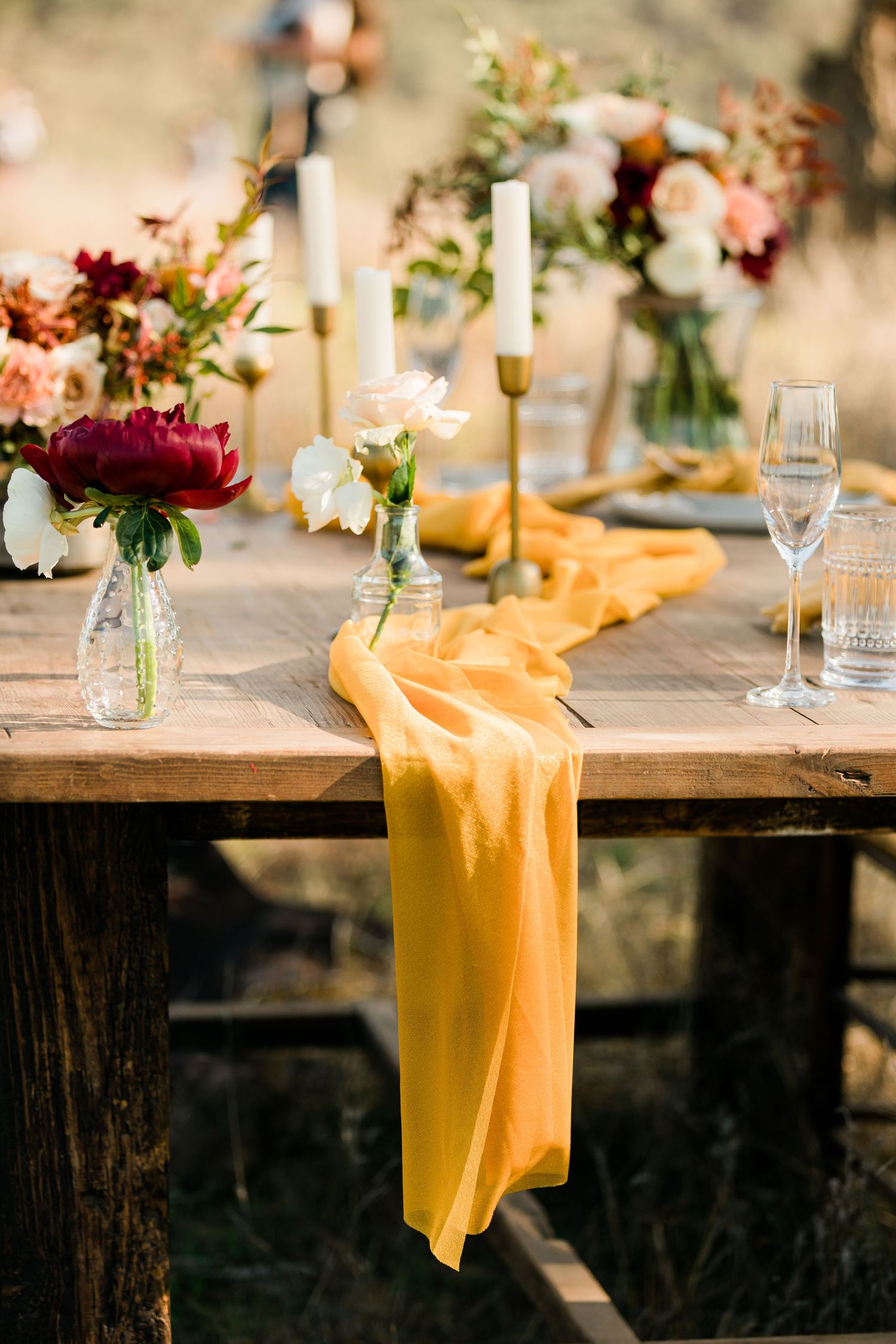 Elegant table setting with yellow runners, floral arrangements and glassware on rustic wooden tables.