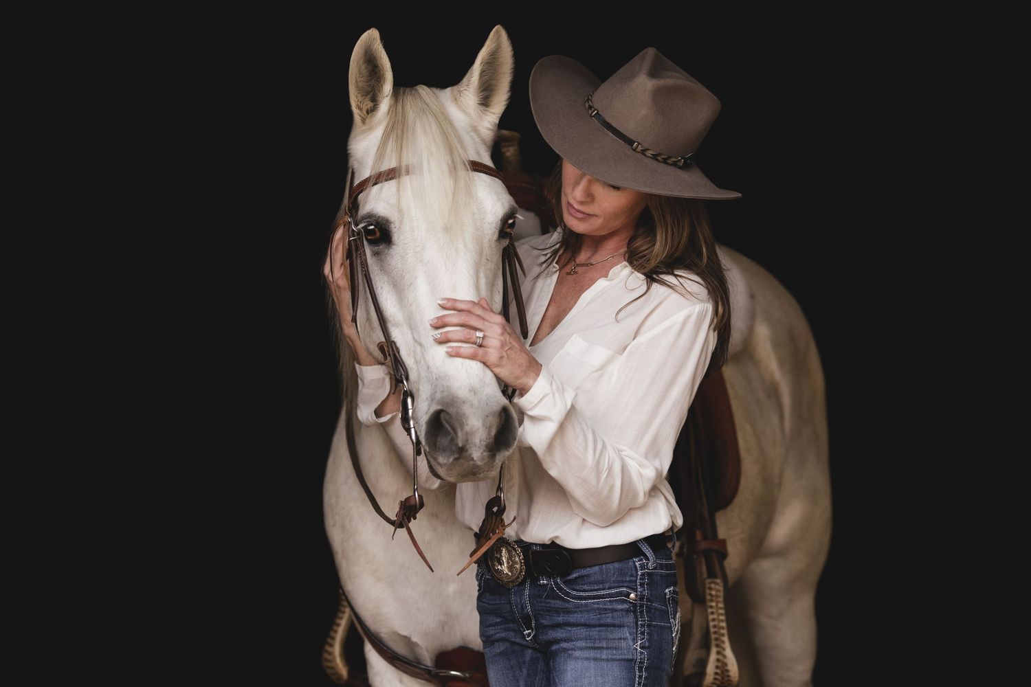 White horse being held by person in western wear against dark background.