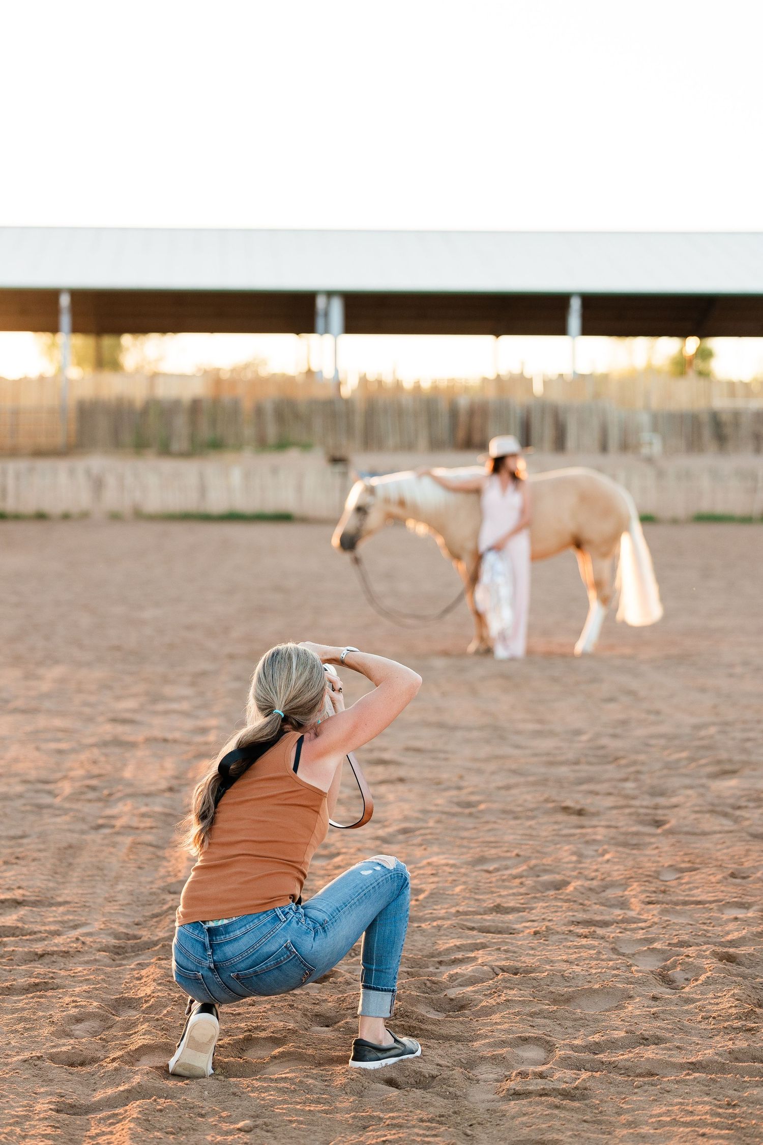 Behind-the-scenes view of a photography session with a horse in a riding arena at sunset.