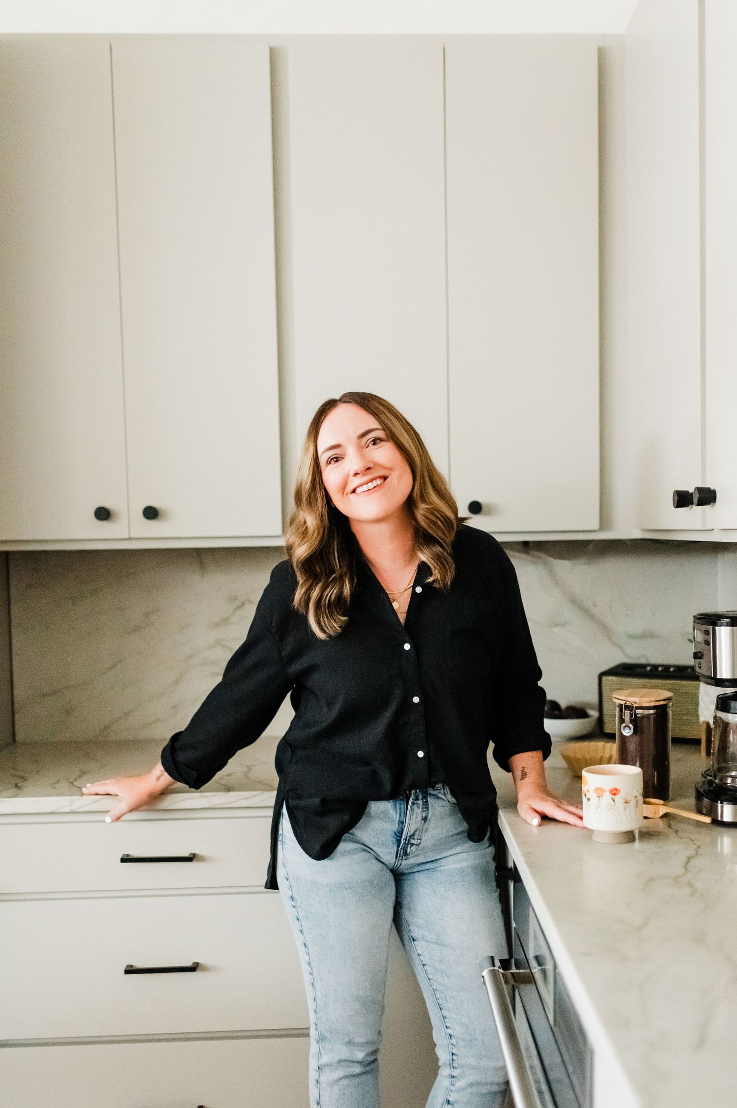 Danielle Miranda, owner of Danielle Miranda Photography, posing confidently in a kitchen wearing a black shirt, radiating a warm, profession