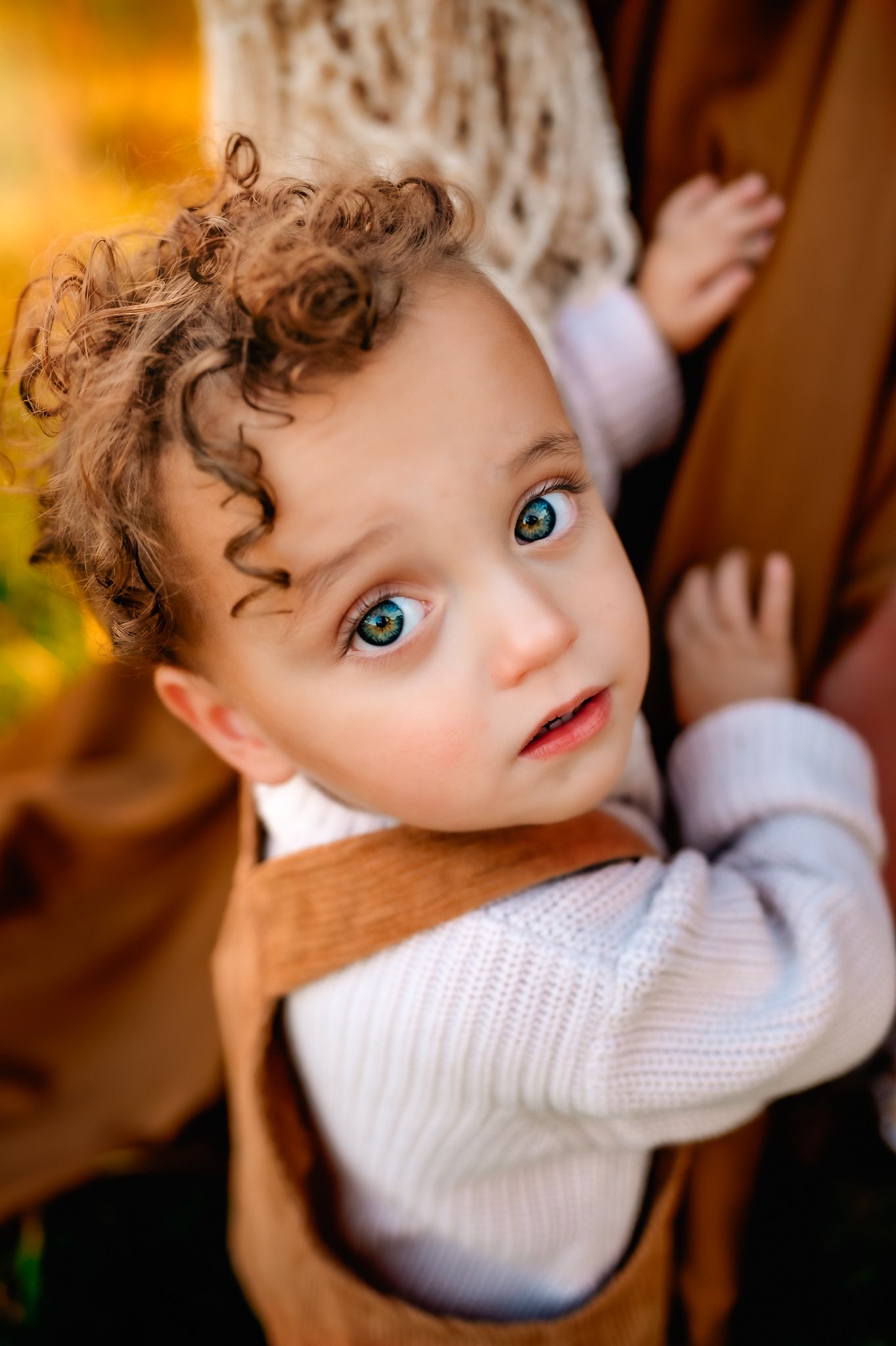 Close up of toddler with curly hair and bright blue eyes wearing white sweater.