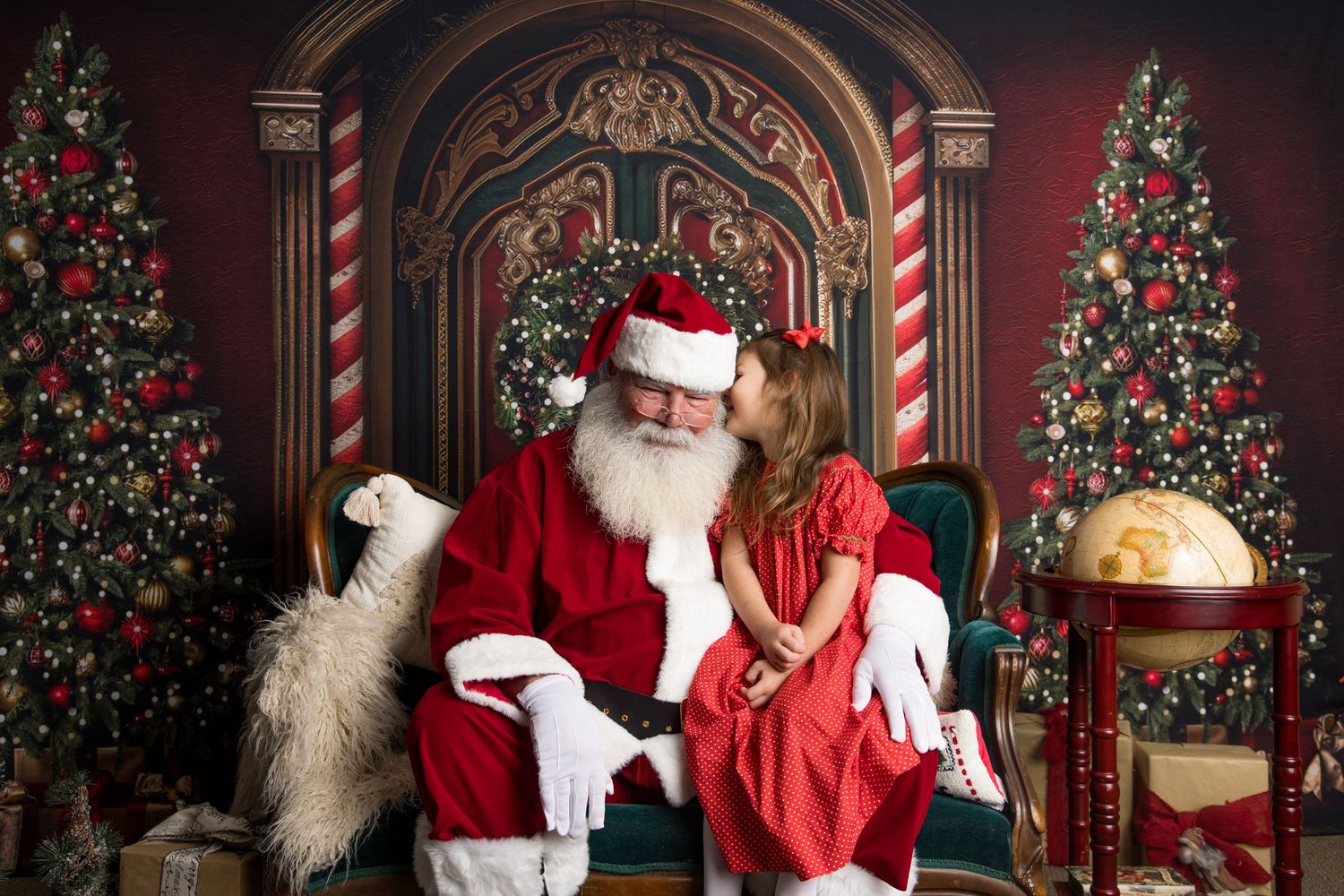Traditional Santa Claus sits in an elegant red and gold Christmas studio setting with decorated trees and candy canes.