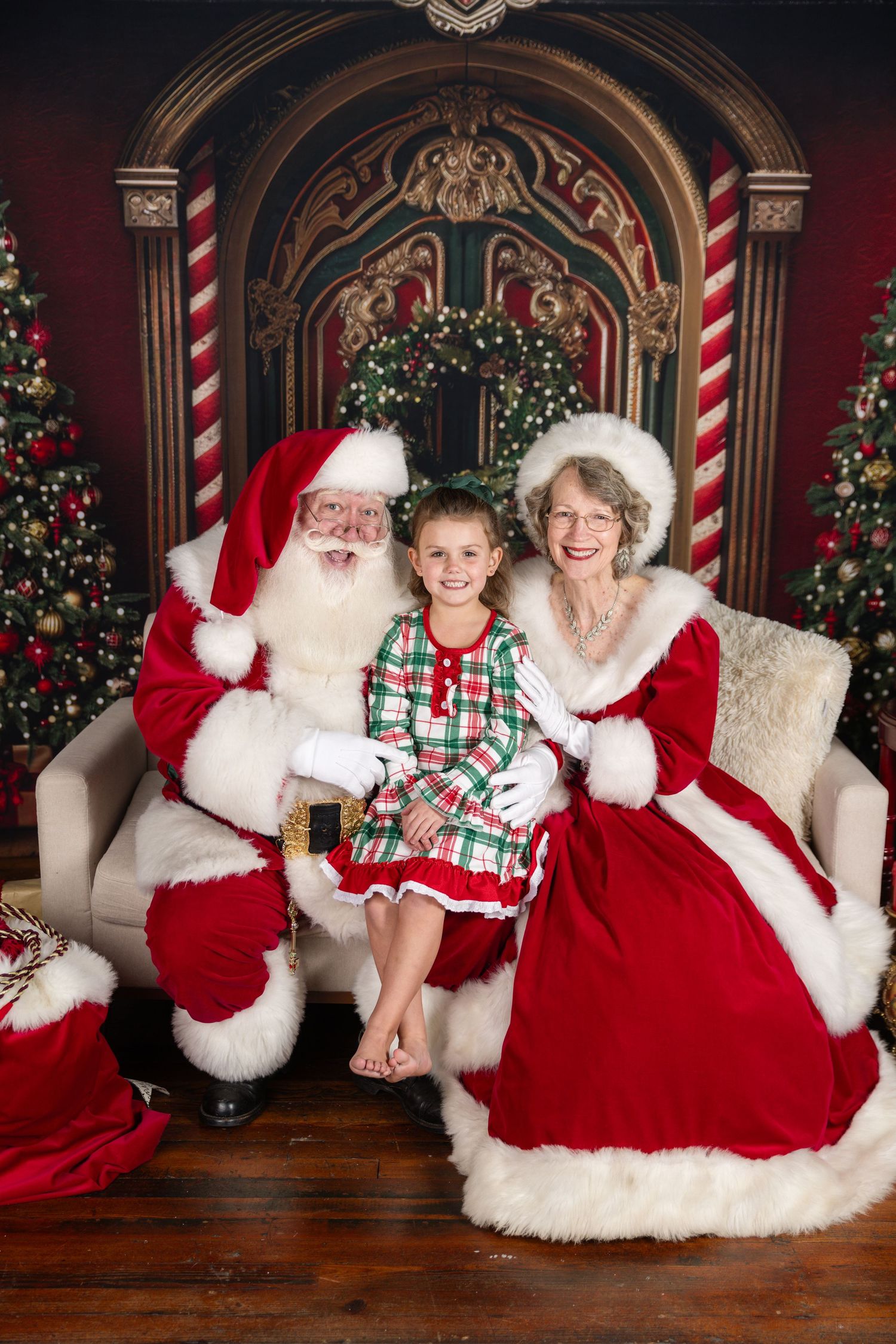 Christmas weekend photo session with Santa and Mrs Claus in a festive holiday setting with decorated trees and striped columns.