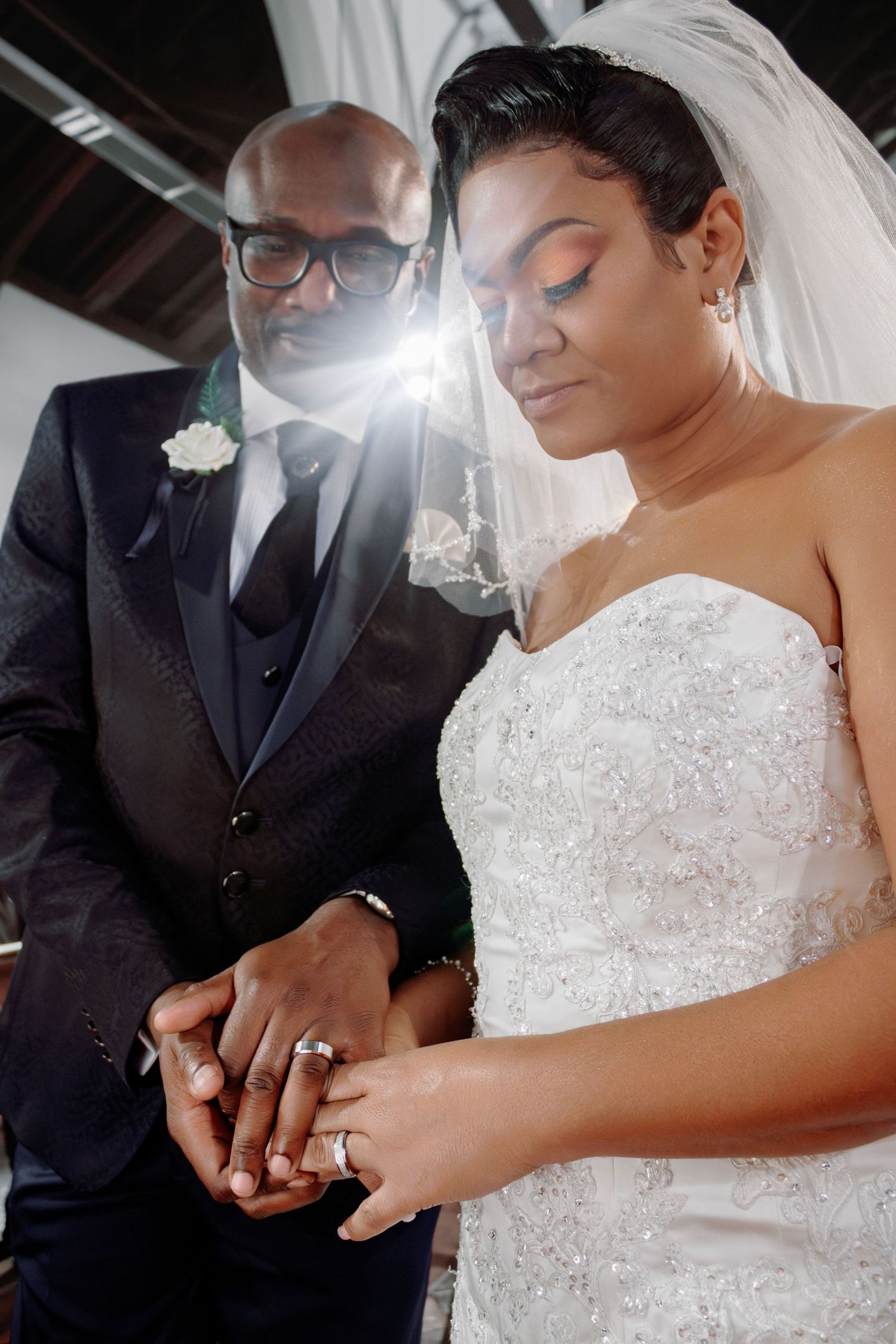 A close-up moment at a wedding ceremony as a couple looks down at their joined hands in elegant attire.