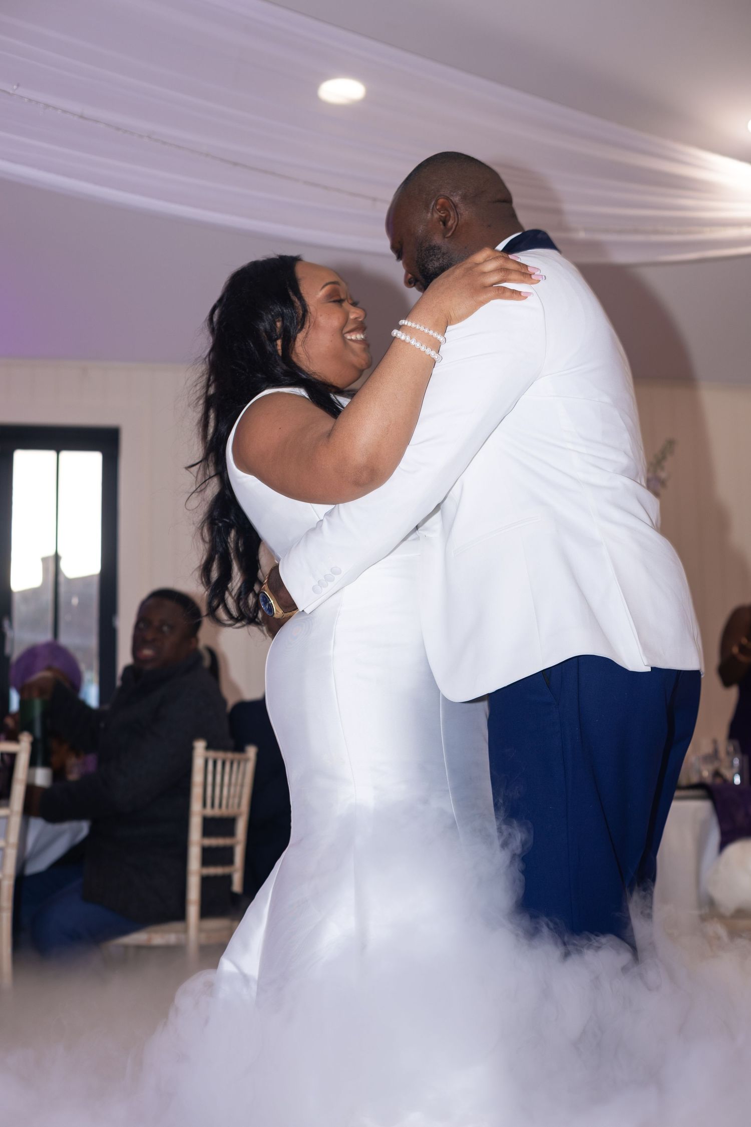 Newlyweds share their first dance amid swirling fog effects on a dance floor at their wedding reception.
