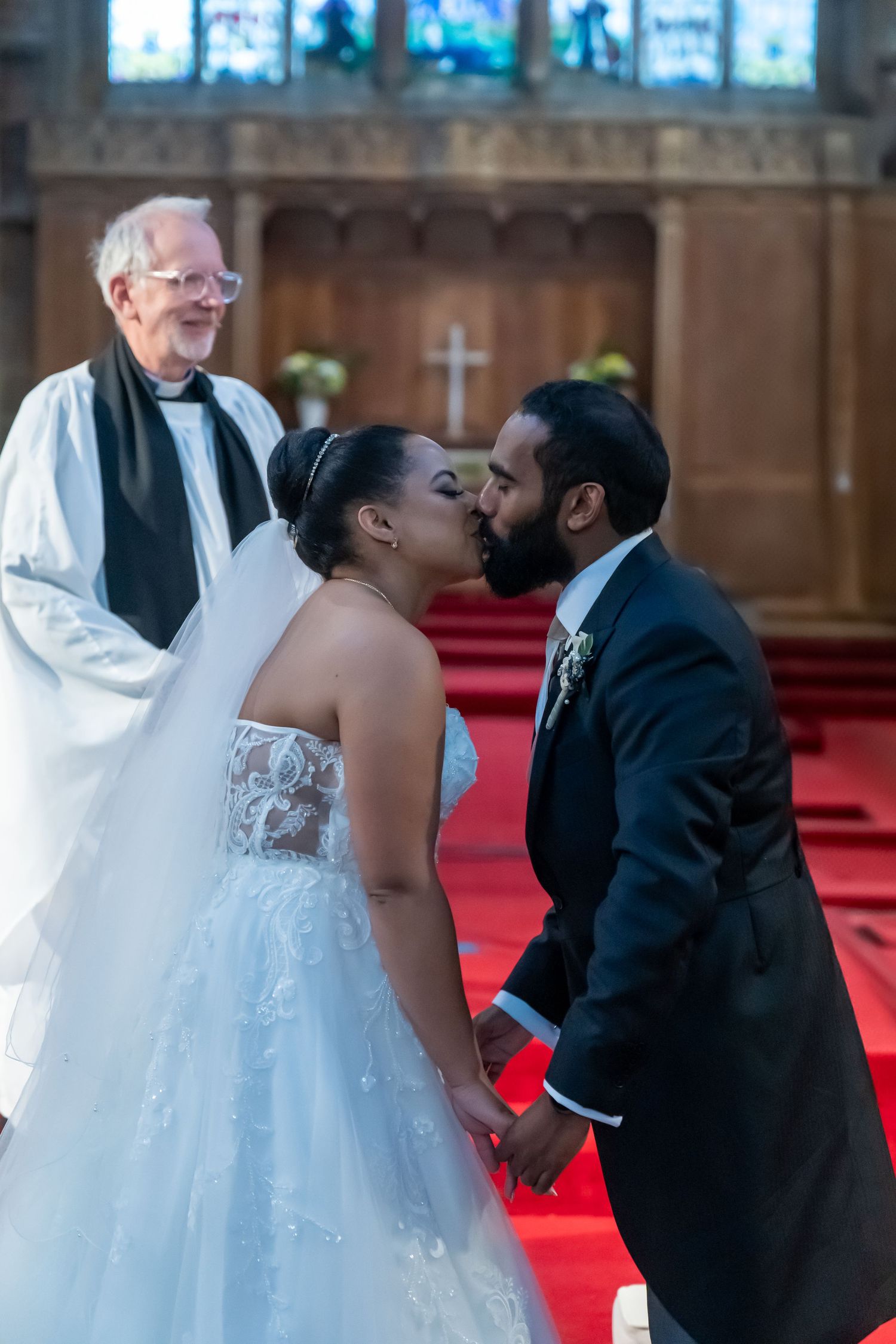 A couple shares their first kiss during a wedding ceremony in a church with a minister standing behind them.