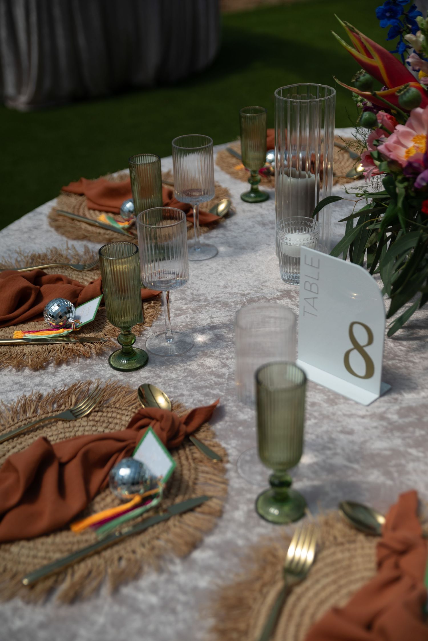 A rustic table setting with green glasses, burlap runner, and white lace tablecloth creates an elegant dining atmosphere.