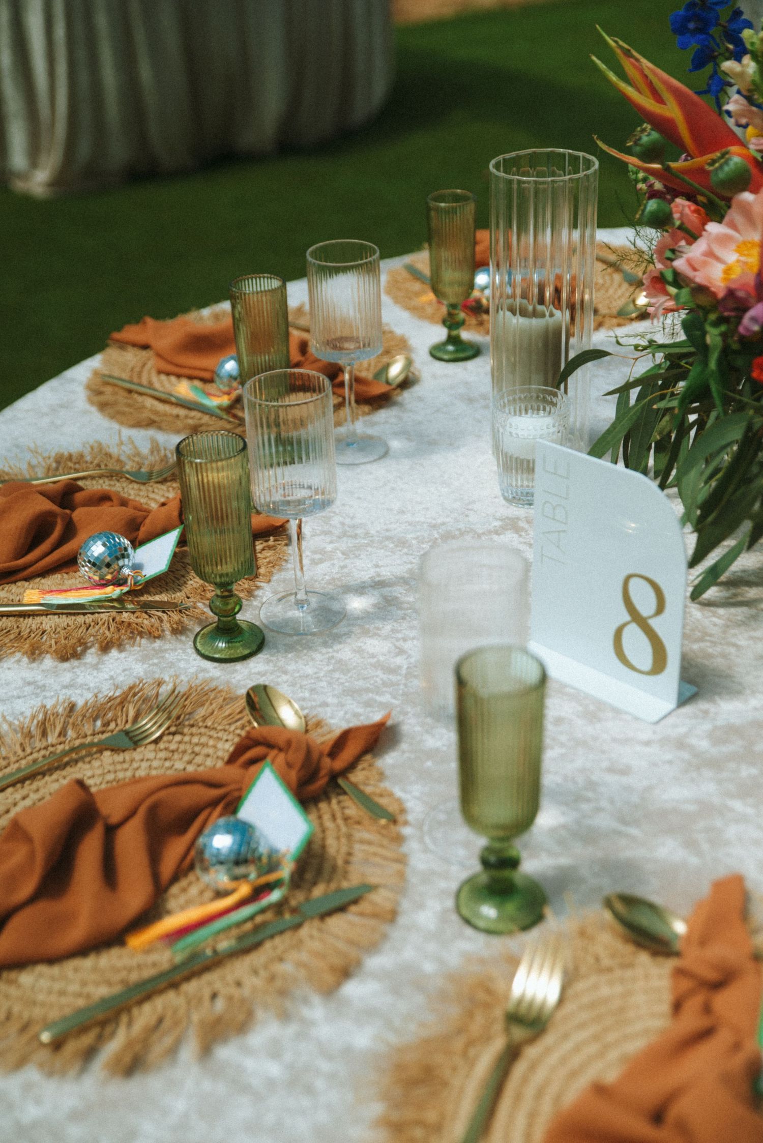 Elegant table setting with green glassware, white tablecloth, terracotta napkins and floral accents for a rustic event.