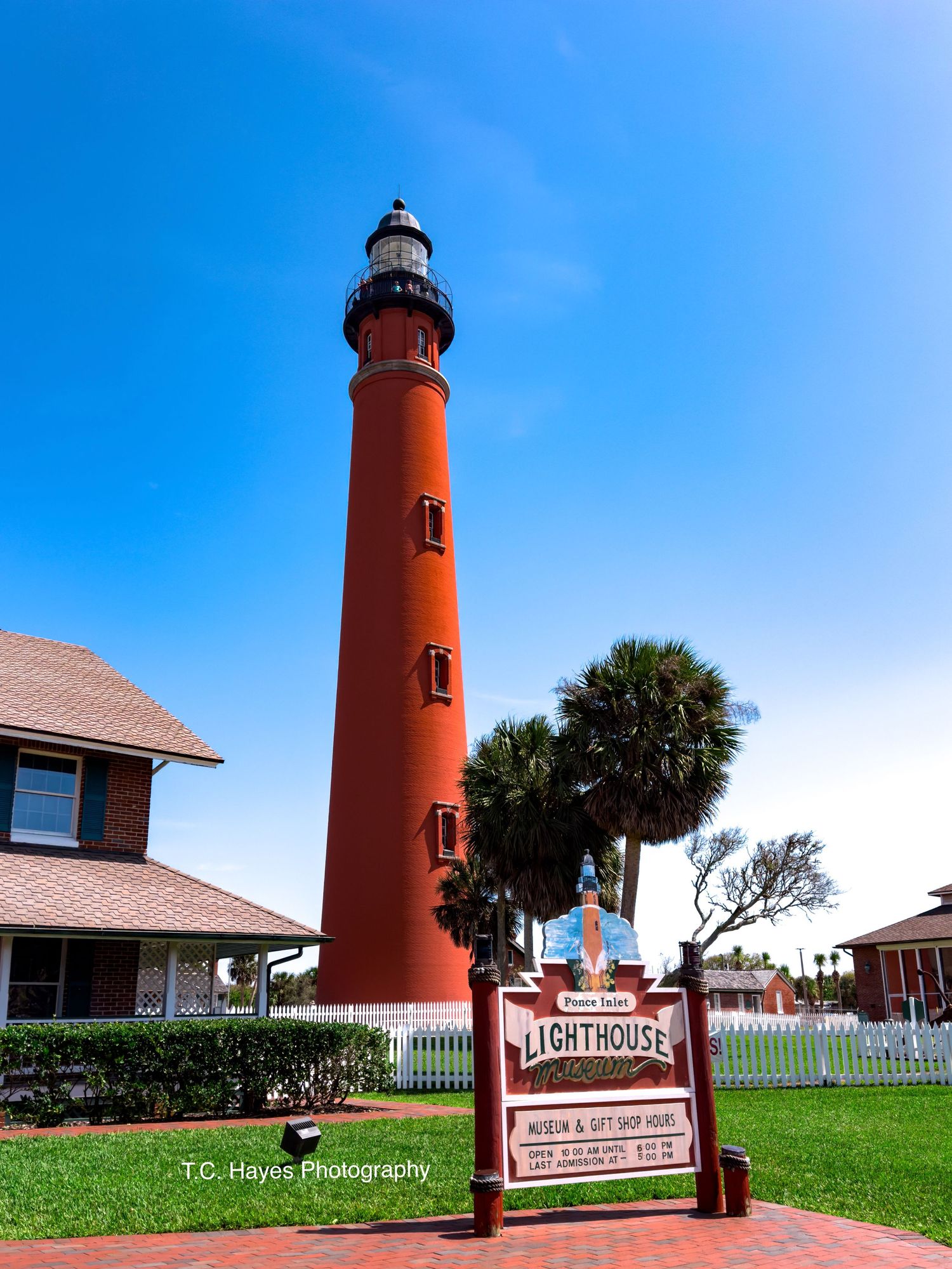 Tall red lighthouse with white trim stands against bright blue sky at Ponce Inlet.