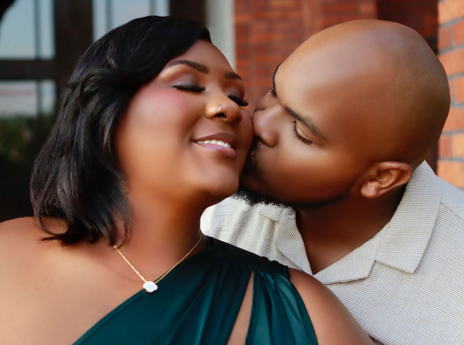Intimate engagement photo of a couple sharing a tender moment against a brick wall.