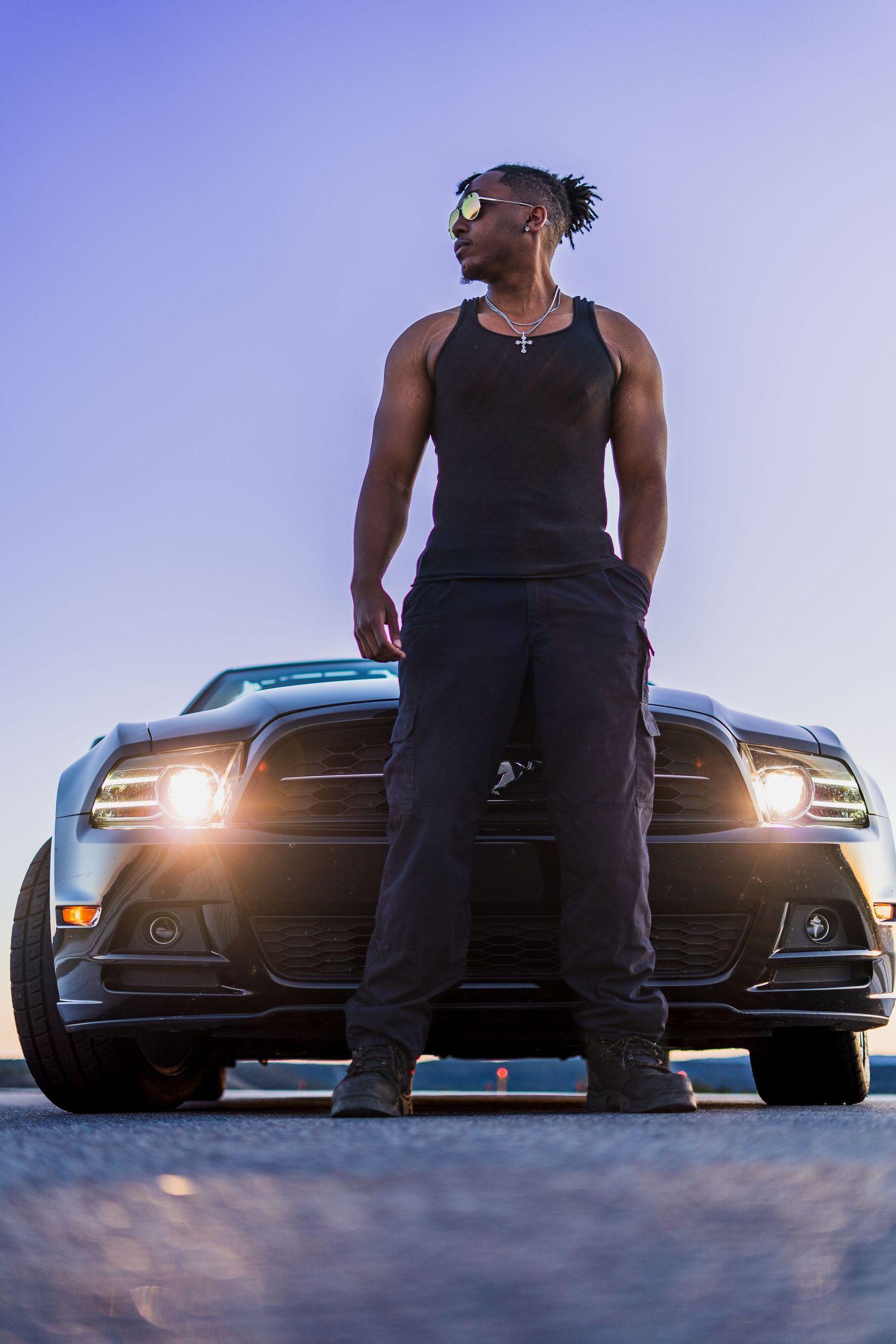 Low-angle silhouette shots of a person standing in front of luxury cars with headlights on at dusk.