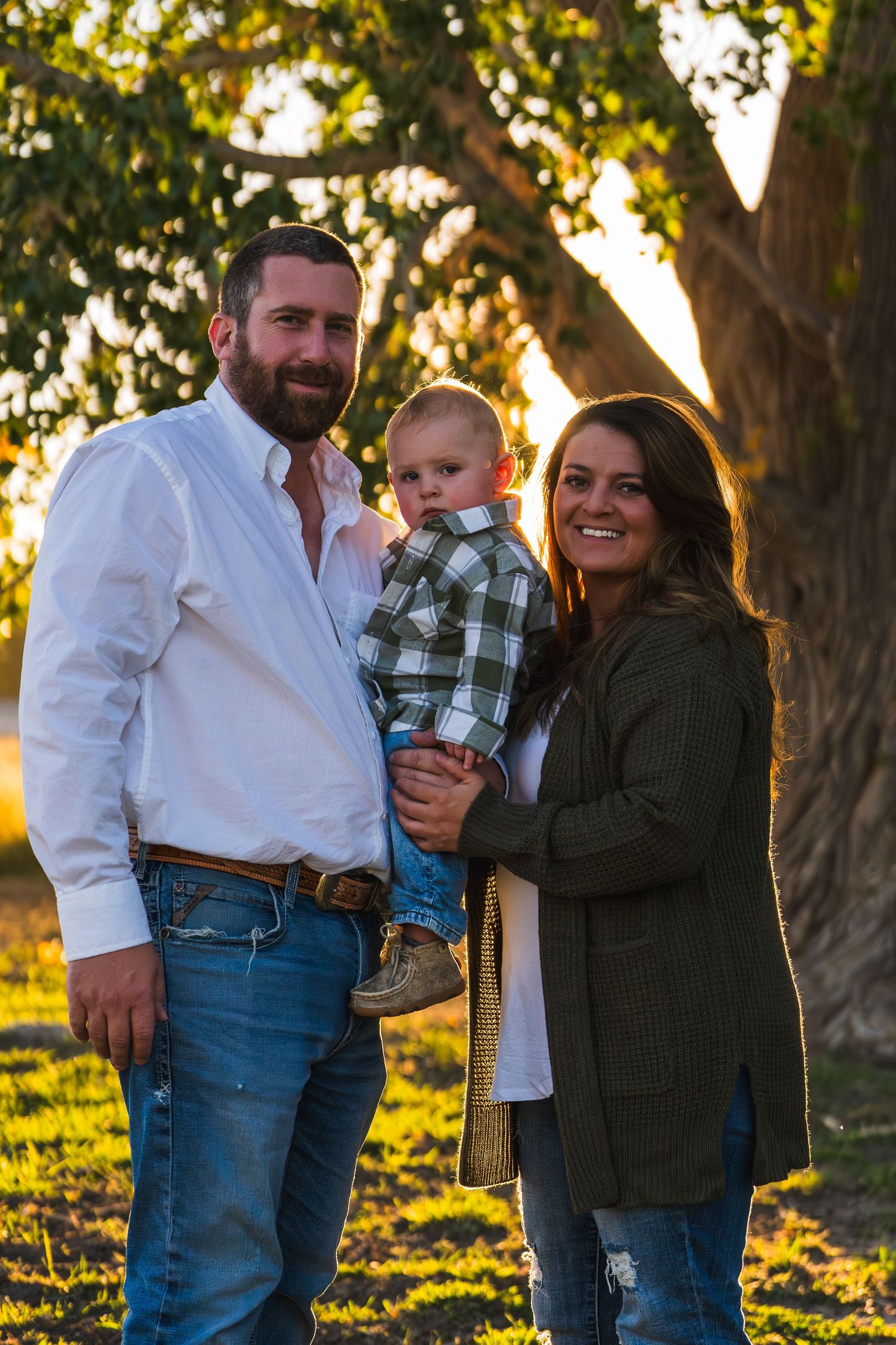 A family poses together outdoors at sunset with golden light filtering through trees in the background.
