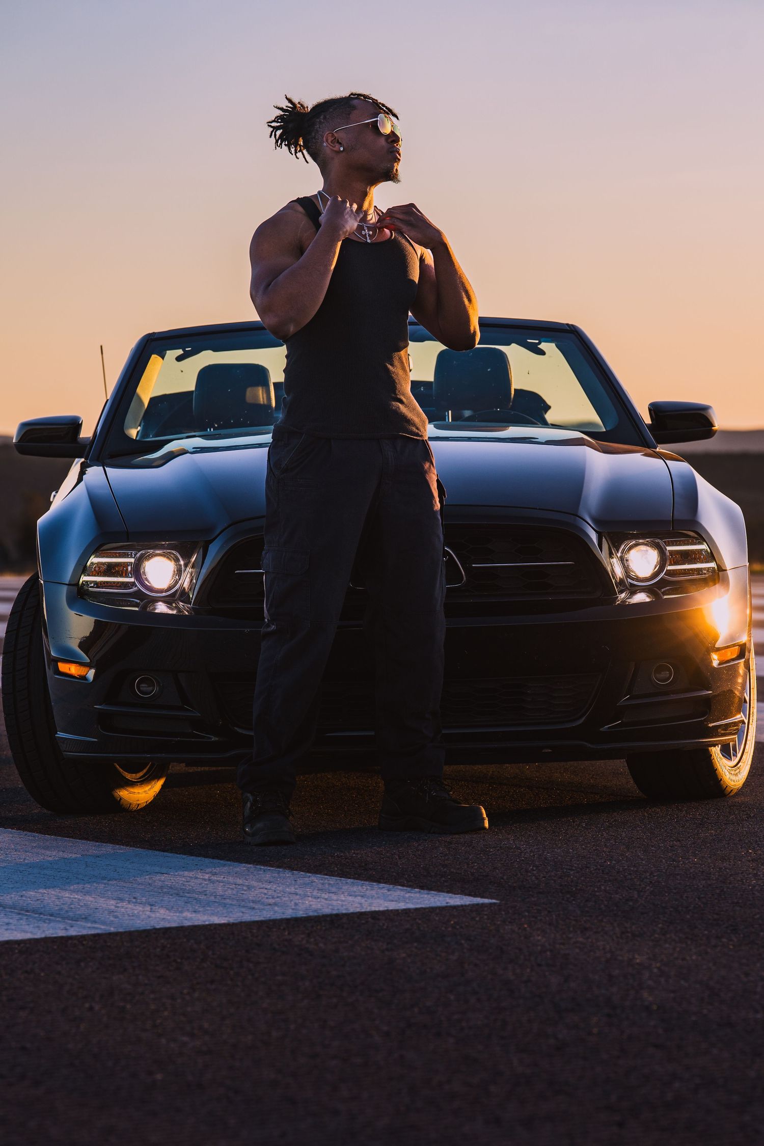 Silhouette of person posing against luxury car at sunset with dramatic lighting and shadows.