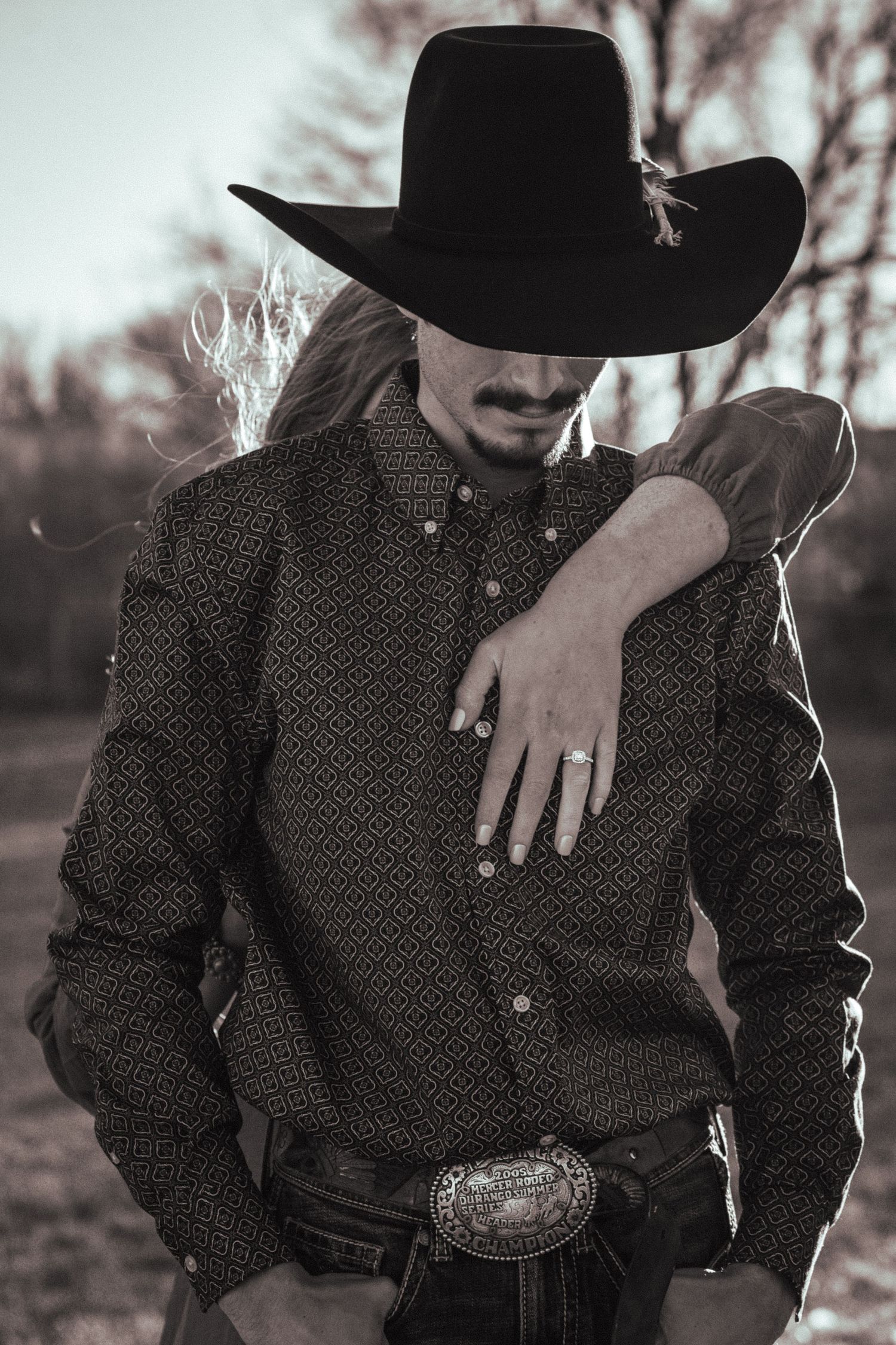 A close-up shot shows someone wearing a black cowboy hat and patterned western shirt with a large belt buckle.