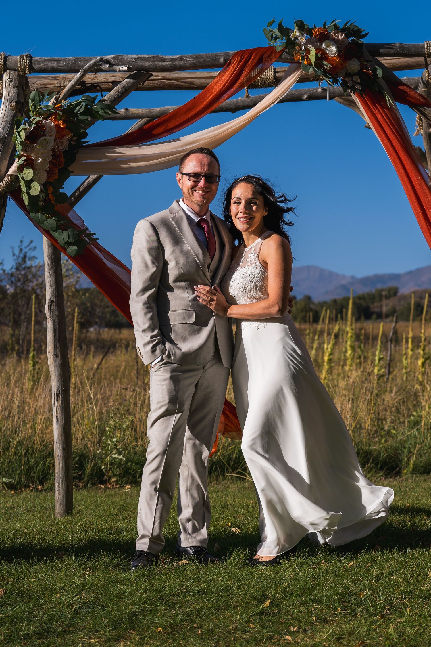 A couple in wedding attire dances together in a scenic outdoor setting with mountains and blue sky in the background.