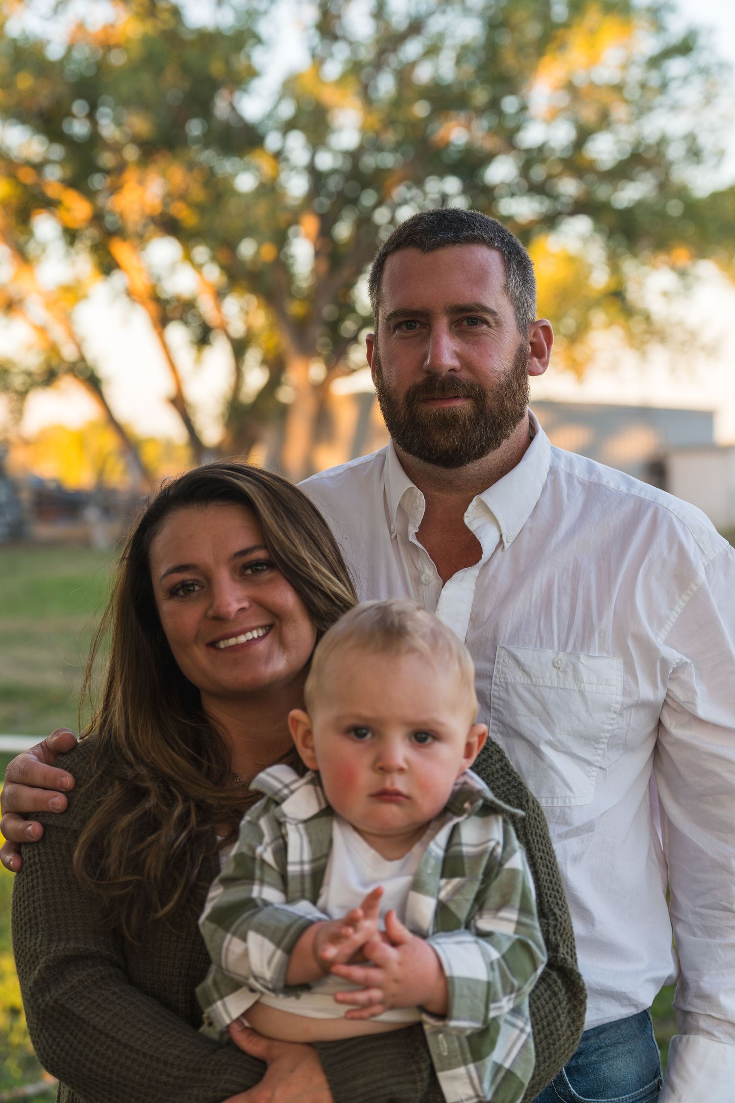 A family poses together outdoors during golden hour with trees and warm sunlight in the background.