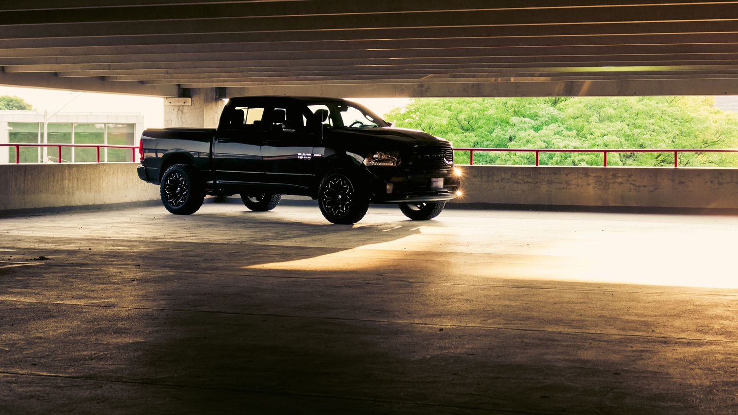A car drives through a dark parking garage creating a dramatic silhouette effect against bright sunlight.