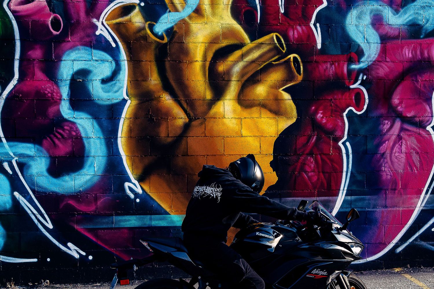 Vibrant street art mural featuring anatomical hearts in yellow and red tones, with a motorcycle parked in front.