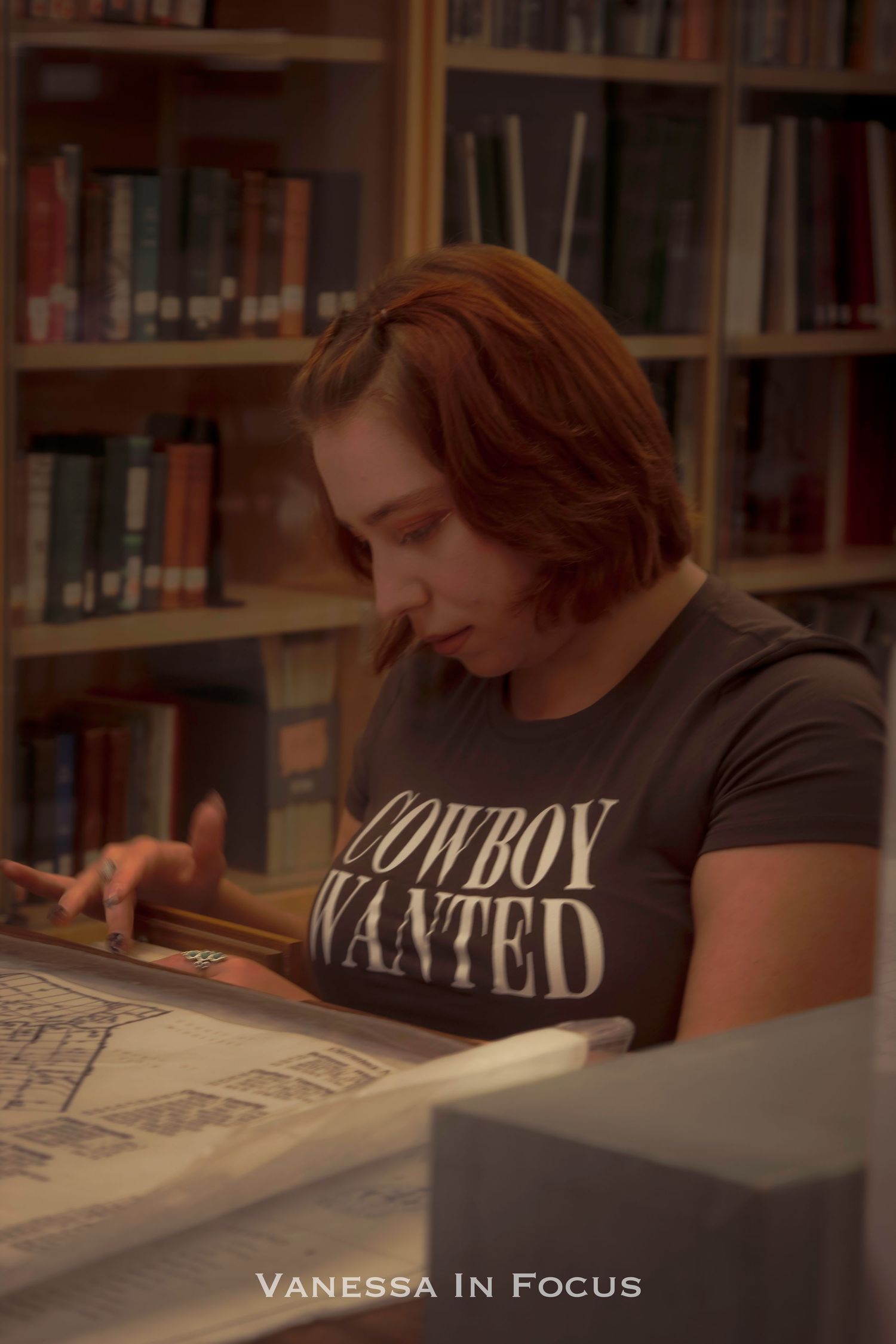 Student wearing black t-shirt studies intently at desk in library with bookshelves in background.