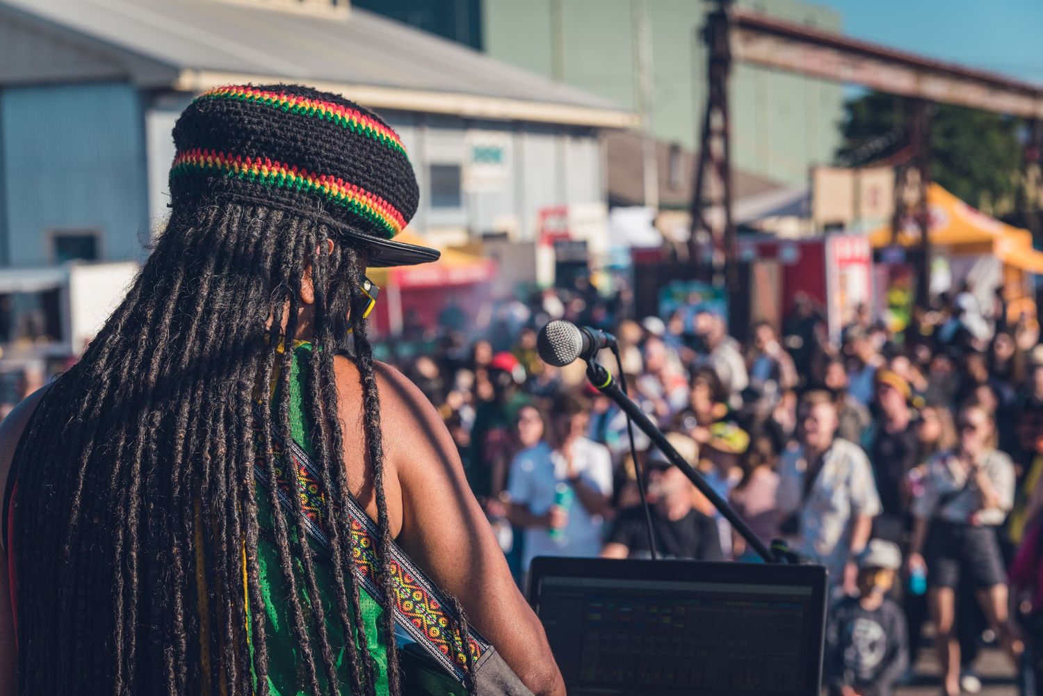 Reggae artist with long braids and colorful Rasta hat performing before large outdoor crowd.