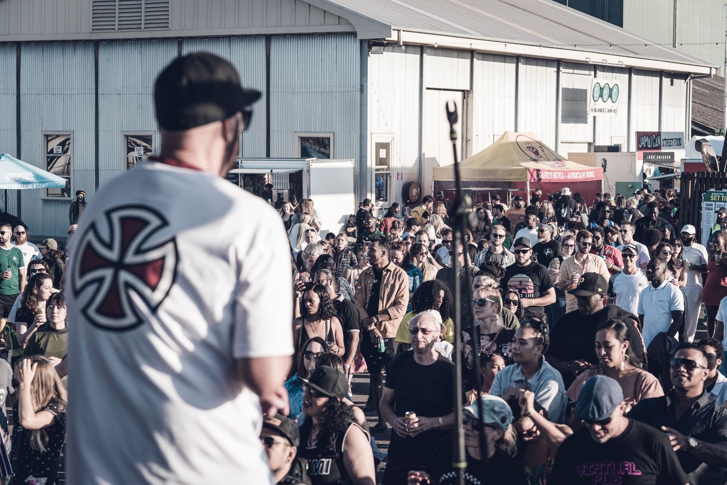 Singer in Independent t-shirt addresses large outdoor festival crowd from stage.