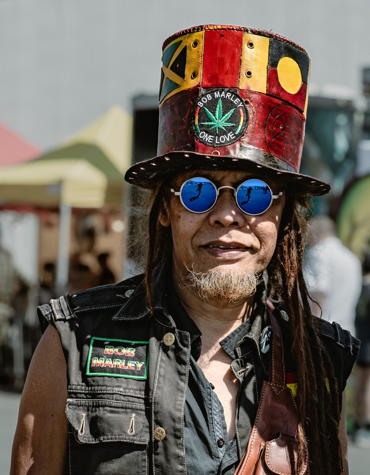Man in Bob Marley top hat and blue mirror sunglasses at reggae festival.