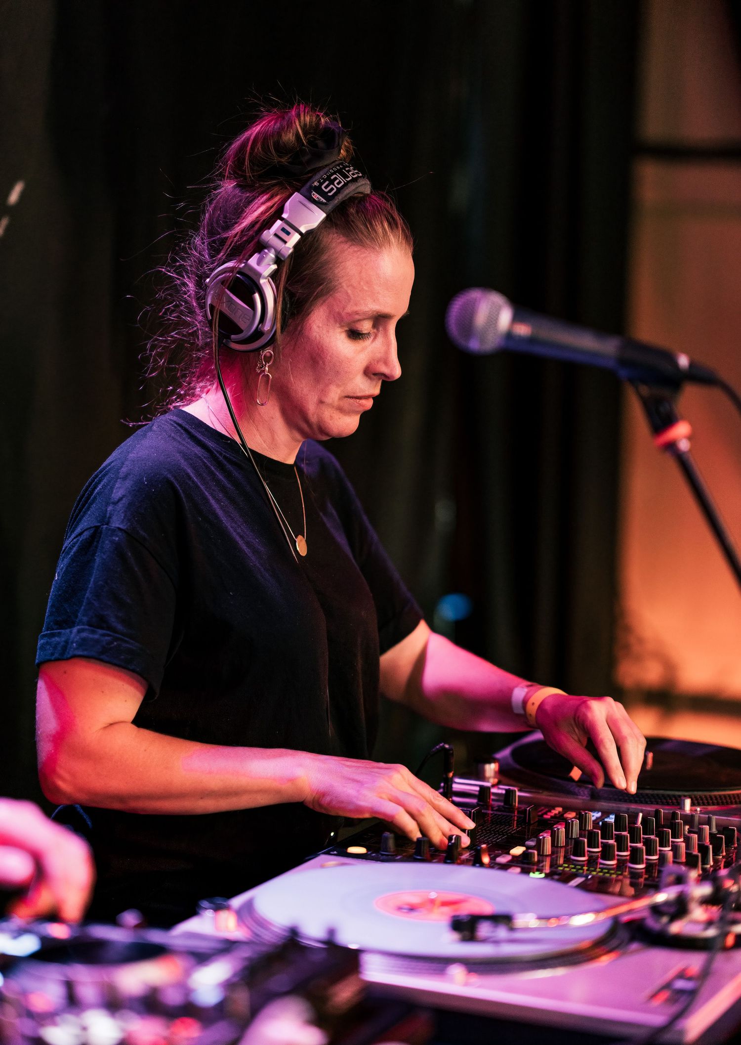Female DJ with headphones mixing on turntables at a live music event.