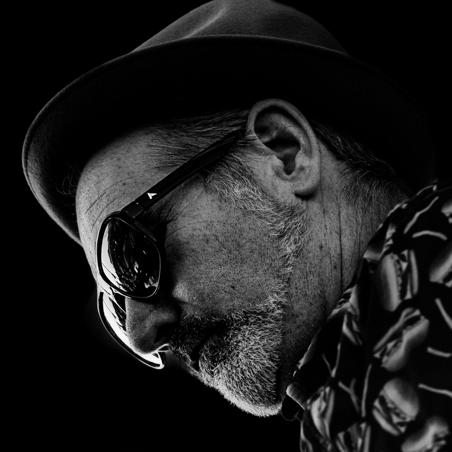 Stylish older man in black hat and sunglasses in black and white portrait.