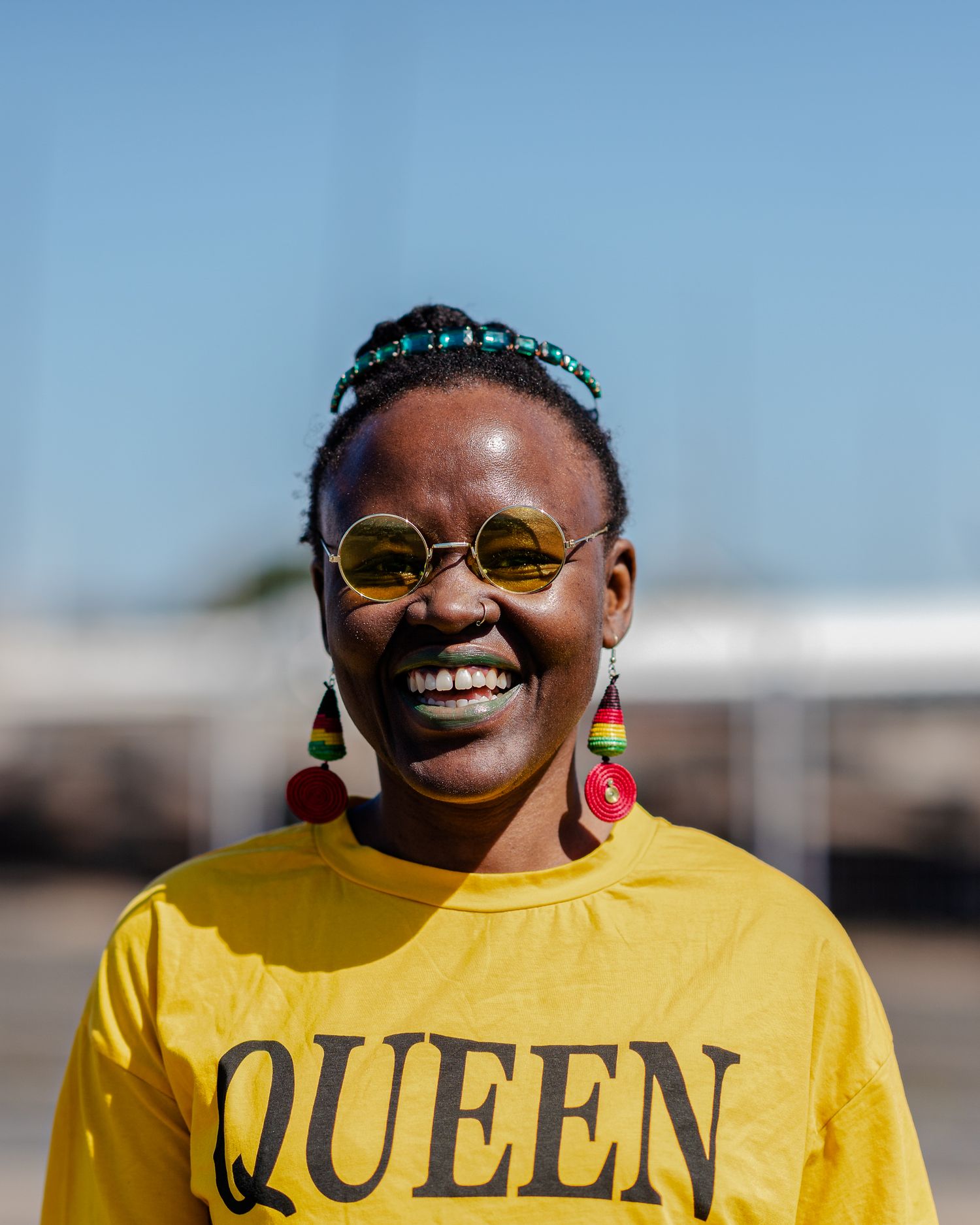 Happy woman in yellow QUEEN shirt with colorful earrings at outdoor event.