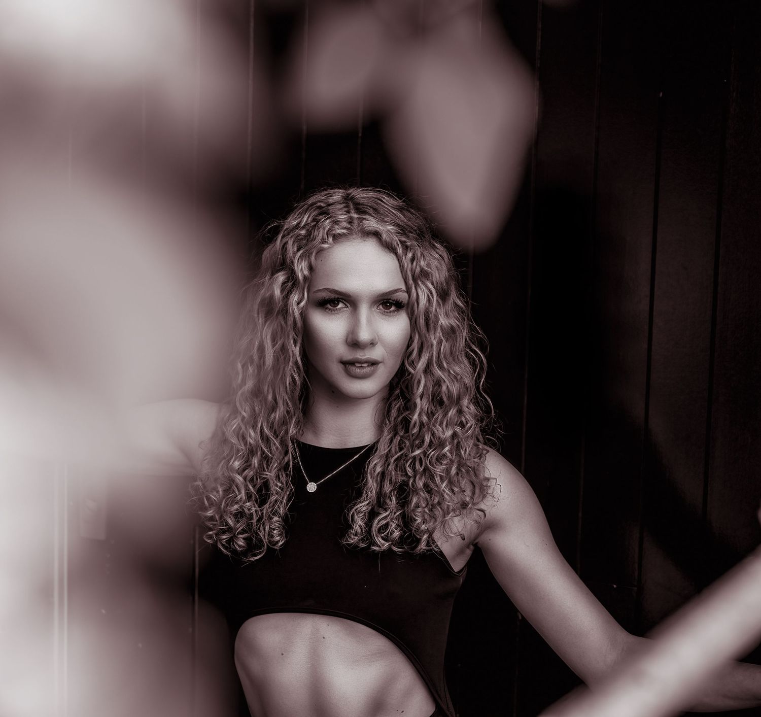 Artistic sepia-toned portrait of a curly-haired woman sitting confidently in atmospheric studio lighting.