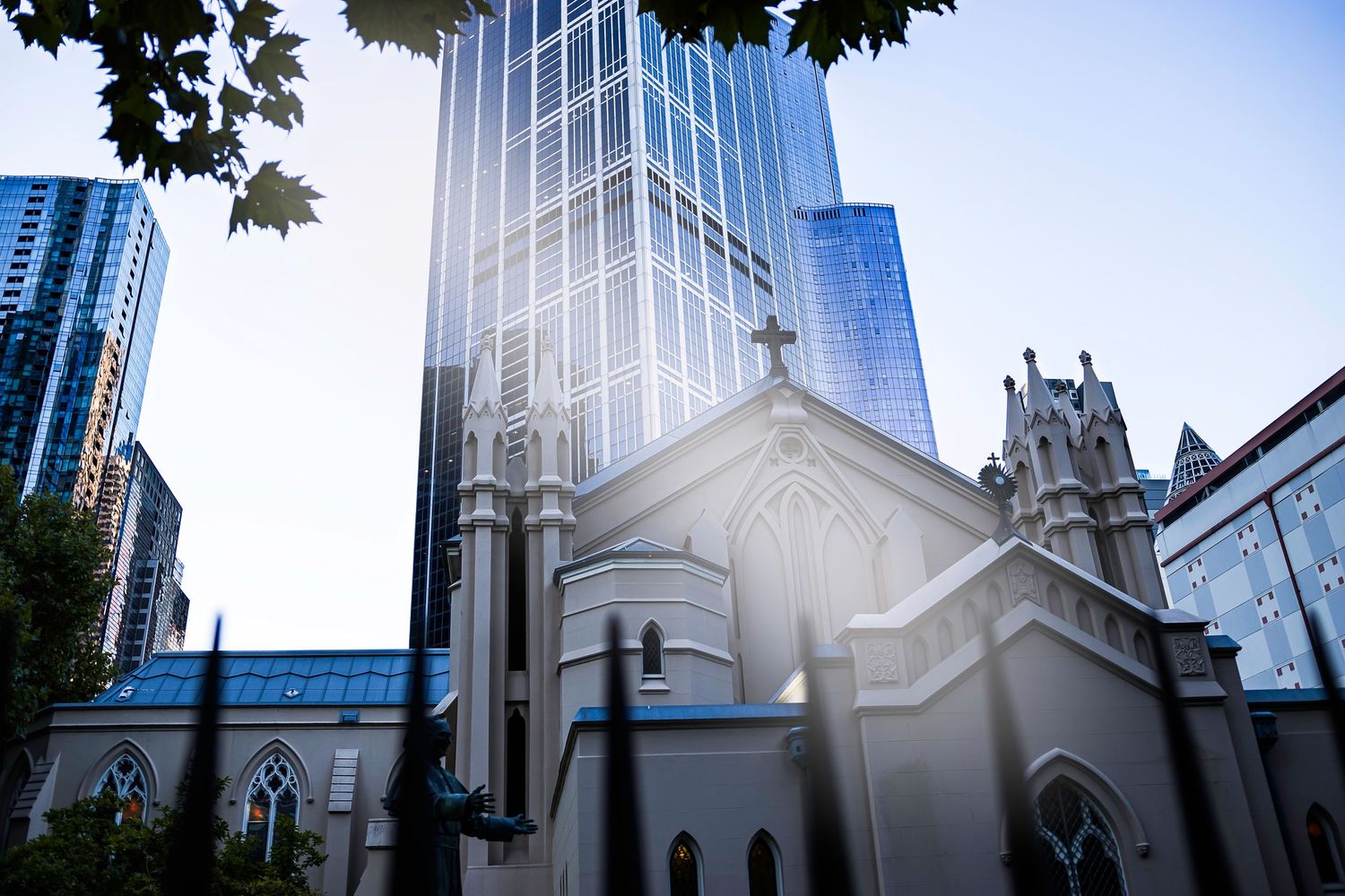 Historic white church contrasts with modern glass skyscrapers in an urban cityscape under a blue sky.