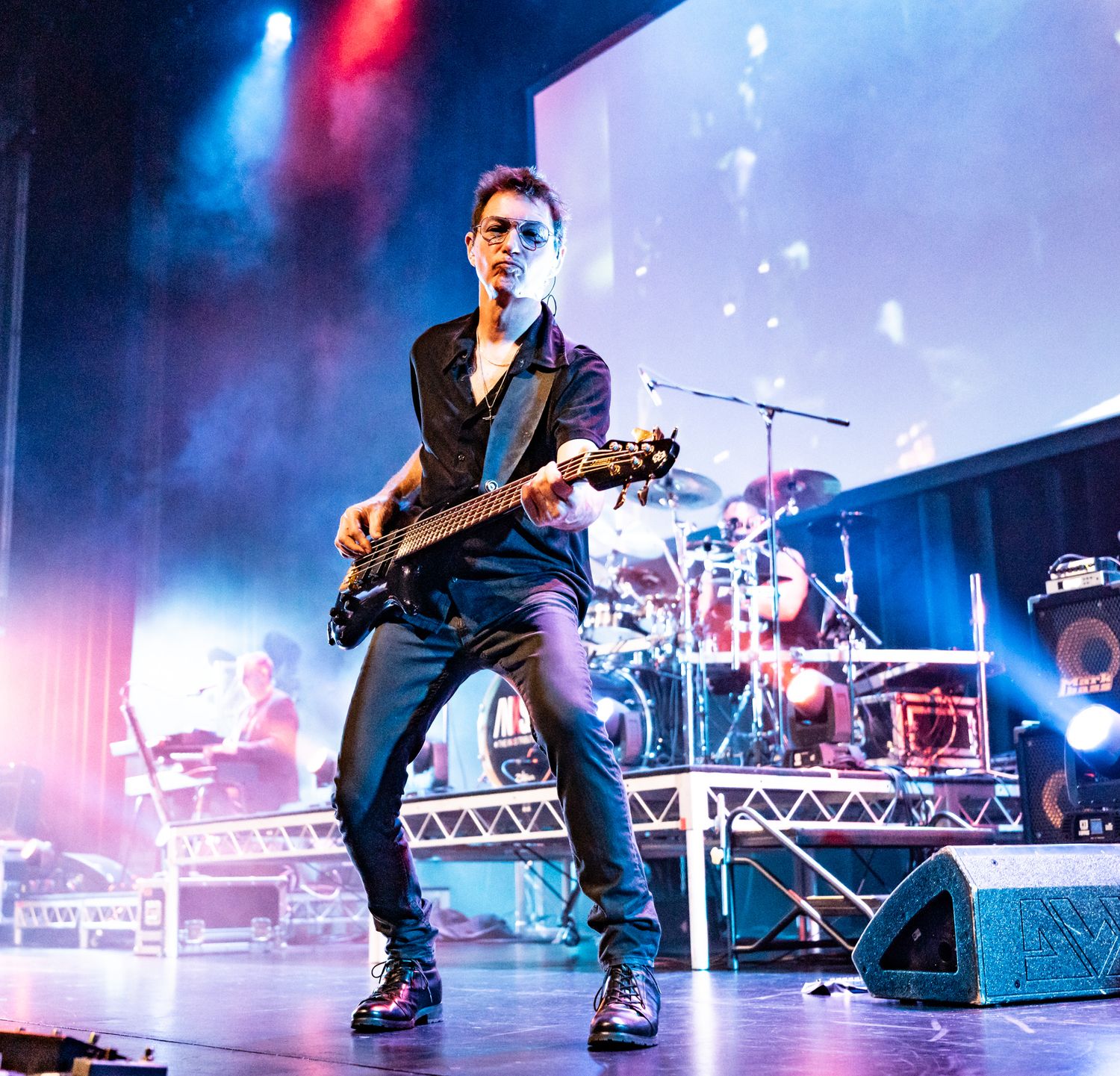 A bassist performs on a dramatically lit stage with blue and pink lighting at a live music event.