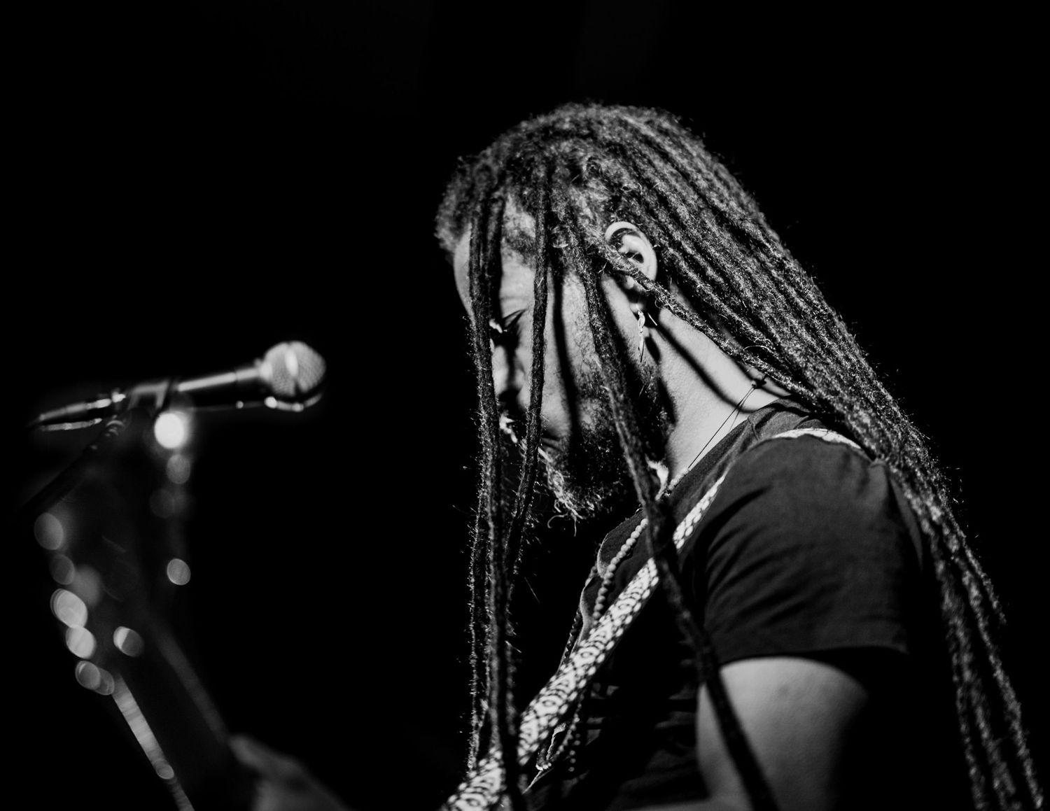 Reggae musician with long dreadlocks performing at microphone on dark stage.