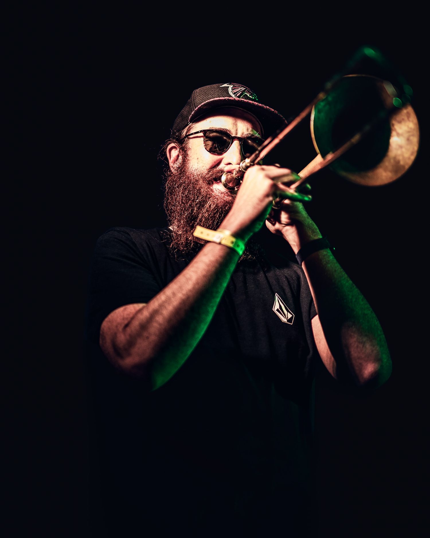 Bearded man playing trombone on stage under green stage lighting.