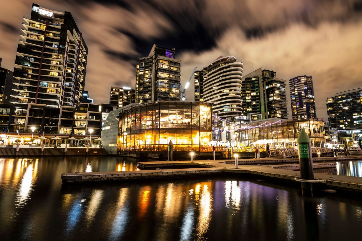 A stunning night cityscape reflects on calm water with illuminated skyscrapers and a waterfront venue.