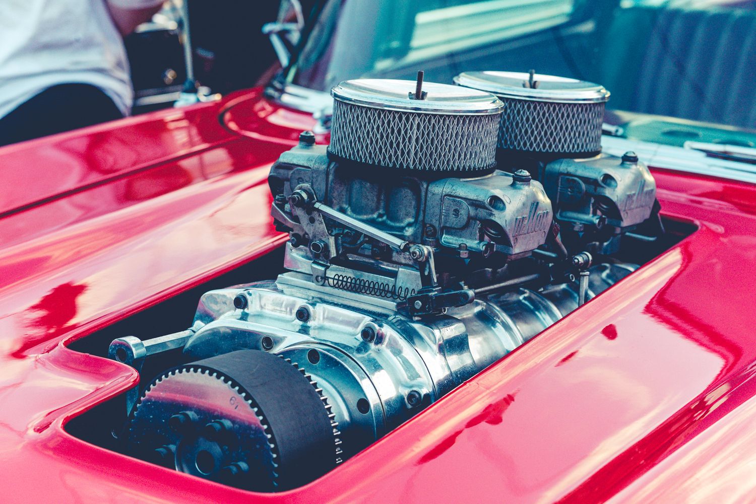 A polished chrome supercharger with dual air filters sits atop a classic red car engine.
