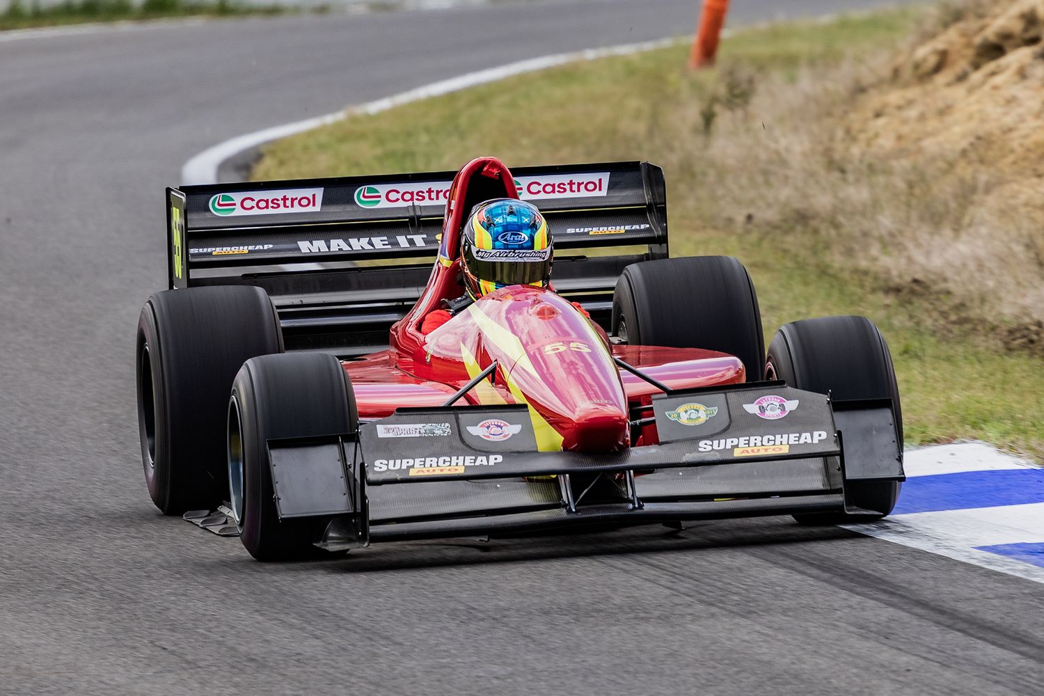 A red Formula racing car speeds around a track with Castrol sponsorship banners visible in the background.
