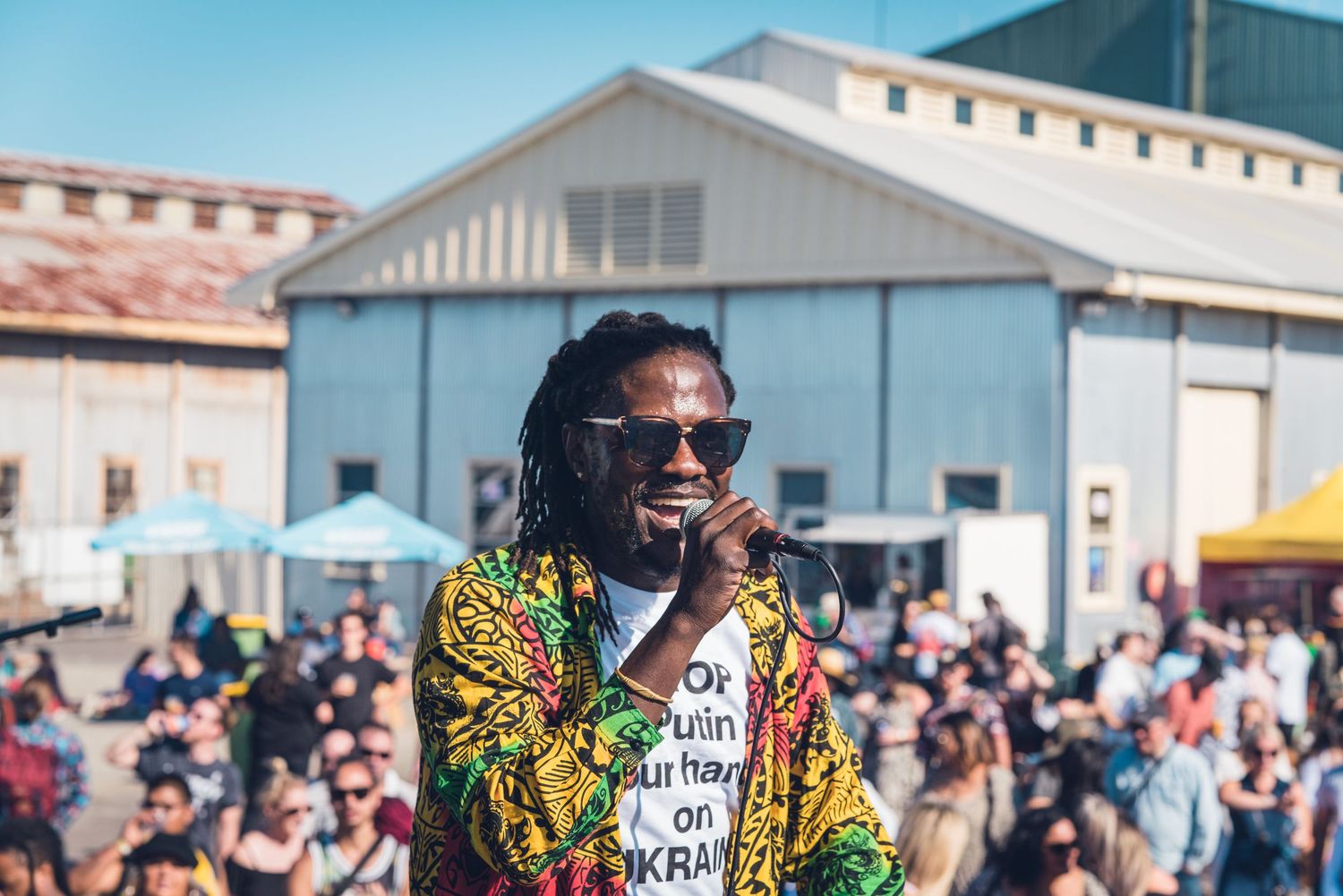 A reggae performer in a vibrant jacket sings to a large crowd at an outdoor Jamaican music festival.