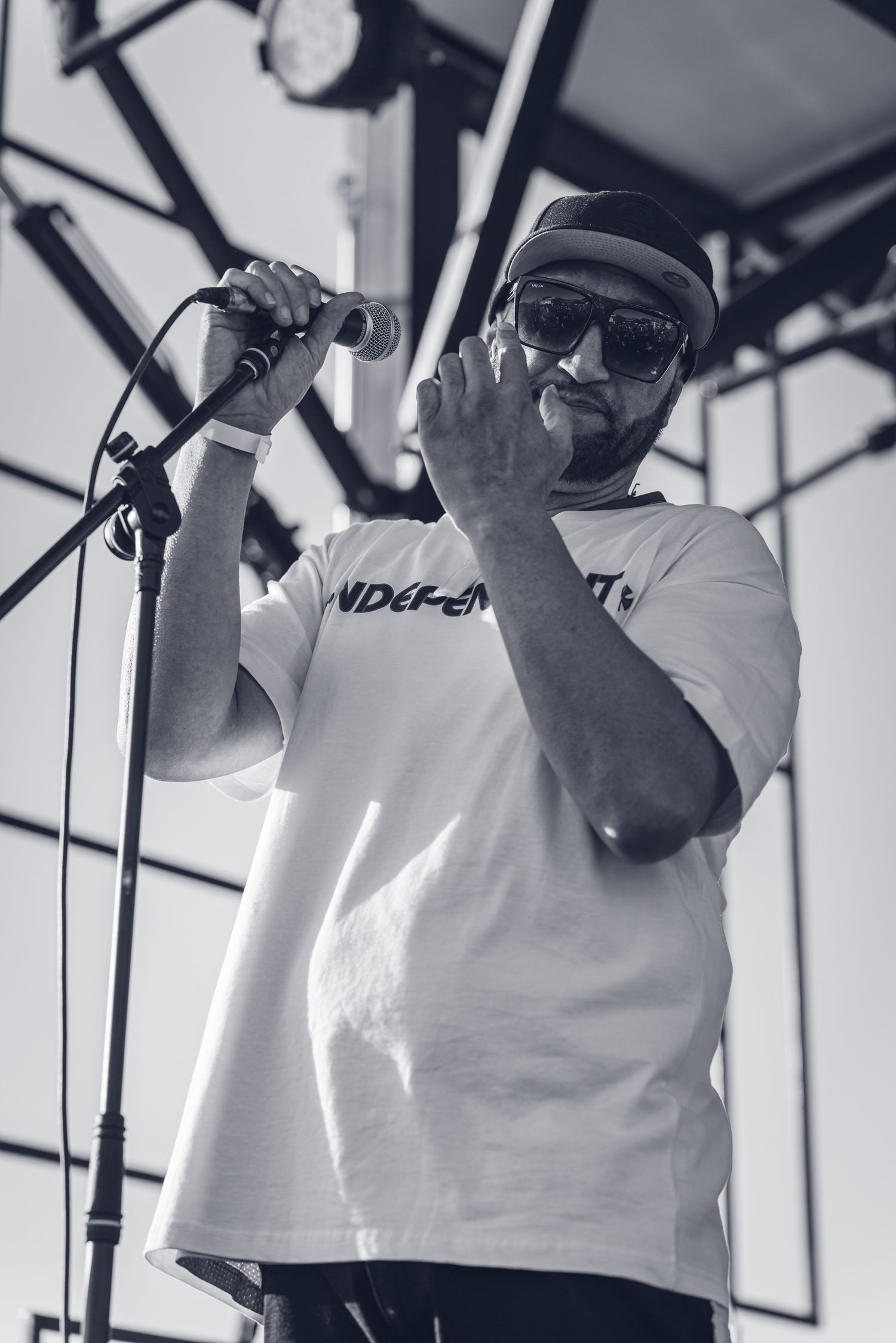 Black and white photo of bearded male performer in white t-shirt singing into microphone on stage.