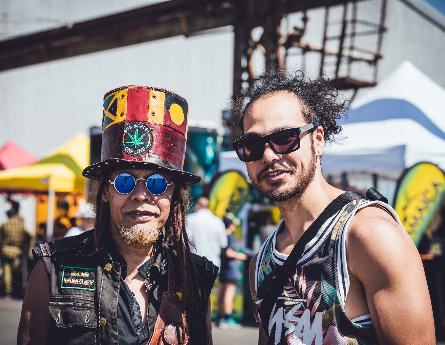 Two men at reggae festival, one wearing colorful Bob Marley top hat.