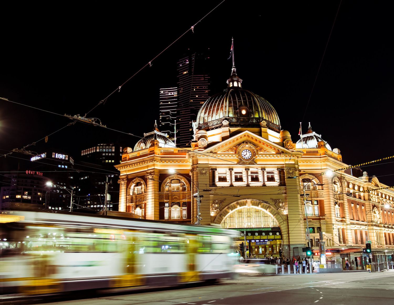 Flinders Street Station illuminated at night with a green tram streaking past in long exposure photography.