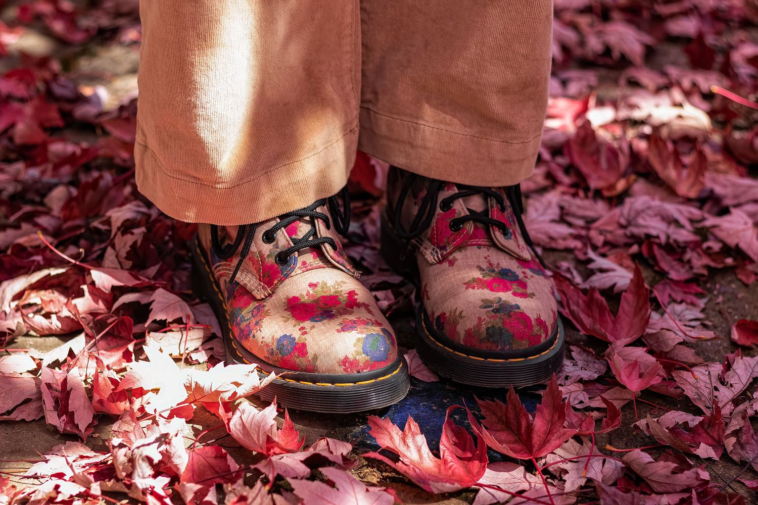 Floral Dr. Martens boots worn over pink trousers standing on a bed of red autumn leaves.
