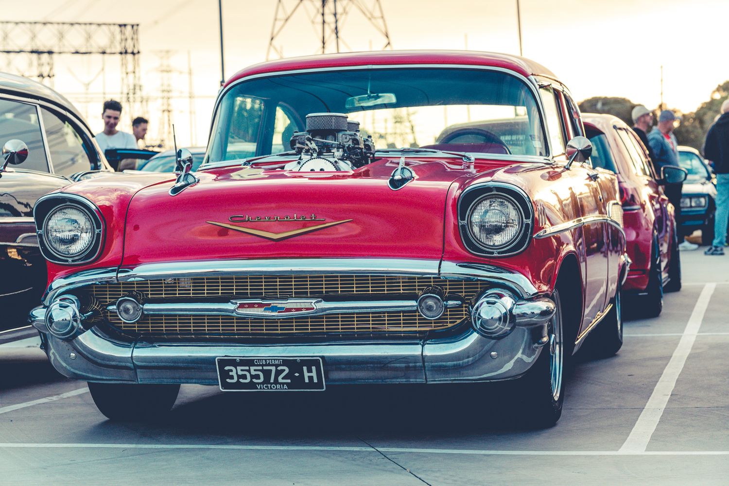 Classic red 1957 Chevrolet Bel Air with supercharged engine on display at an outdoor car show.